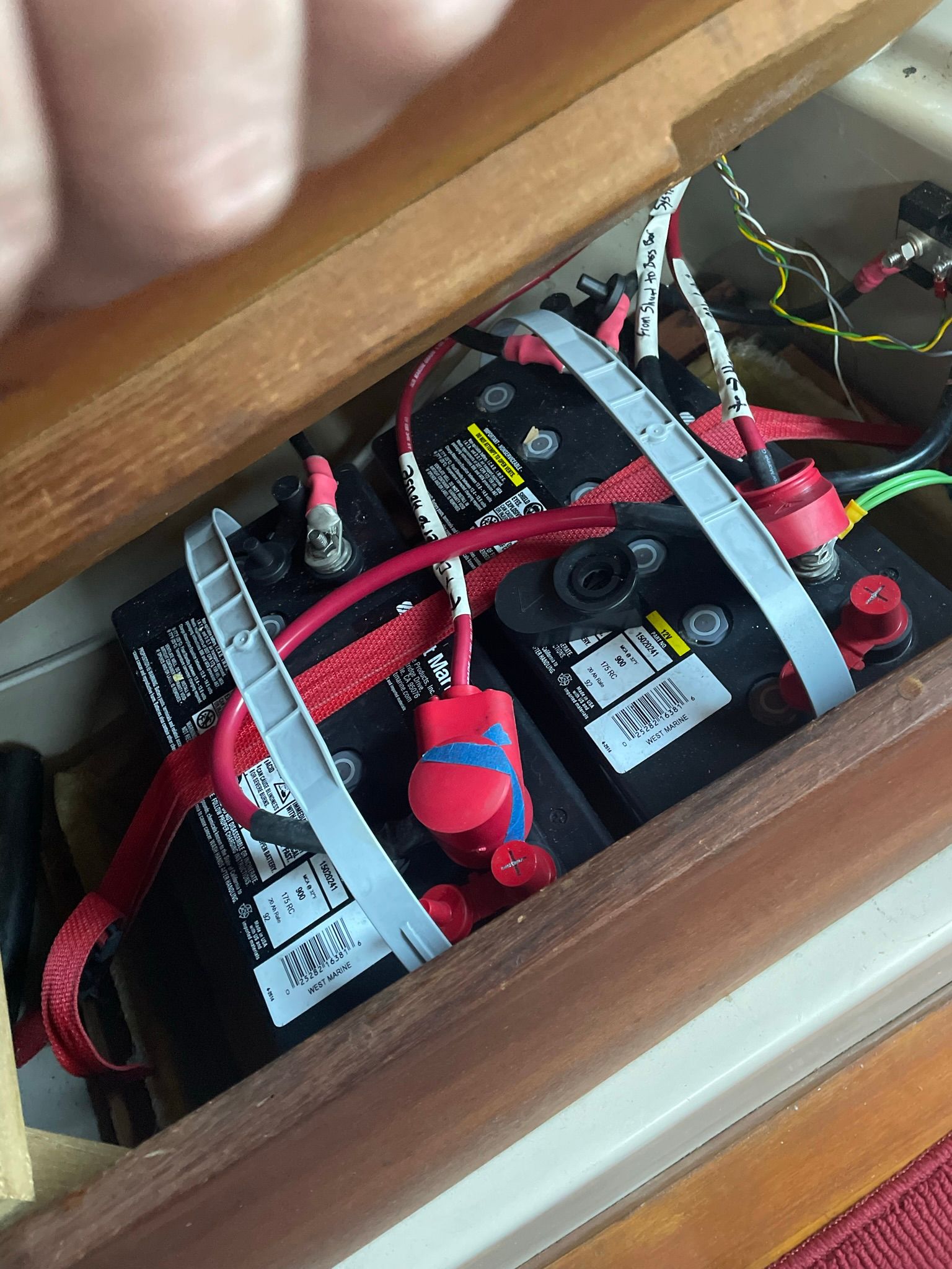 Batteries in a boat with red and black cables, secured by metal straps.