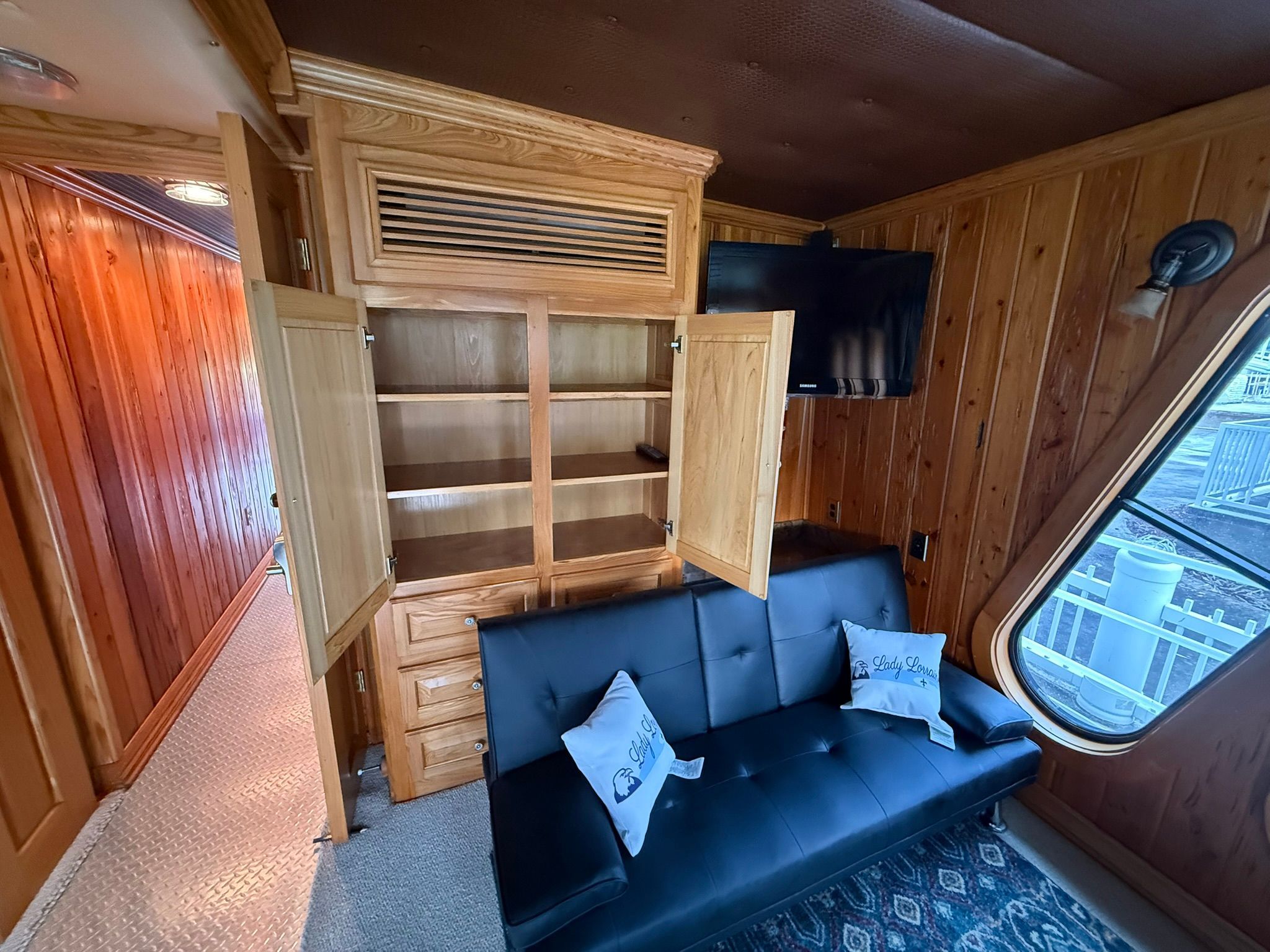 Interior of a boat with wooden walls, a black sofa, and a TV.
