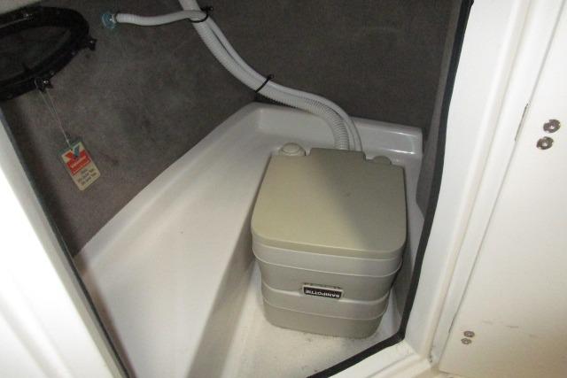 Portable toilet in 2004 Stingray 240 LR boat compartment with plumbing hoses.