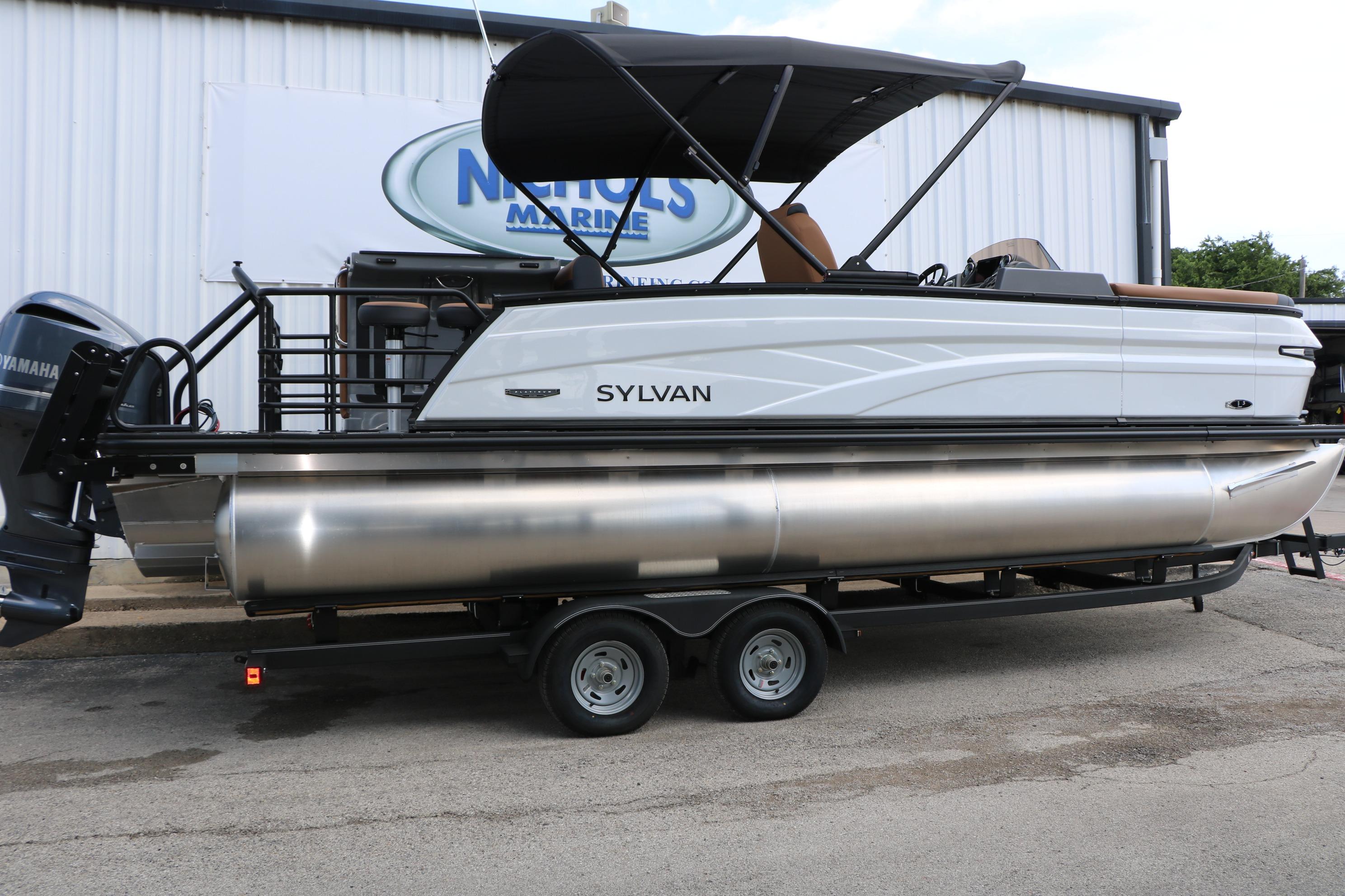 2026 Sylvan L3 DLZ Bar Platinum Edition Tri-Toon boat on trailer outside dealership.