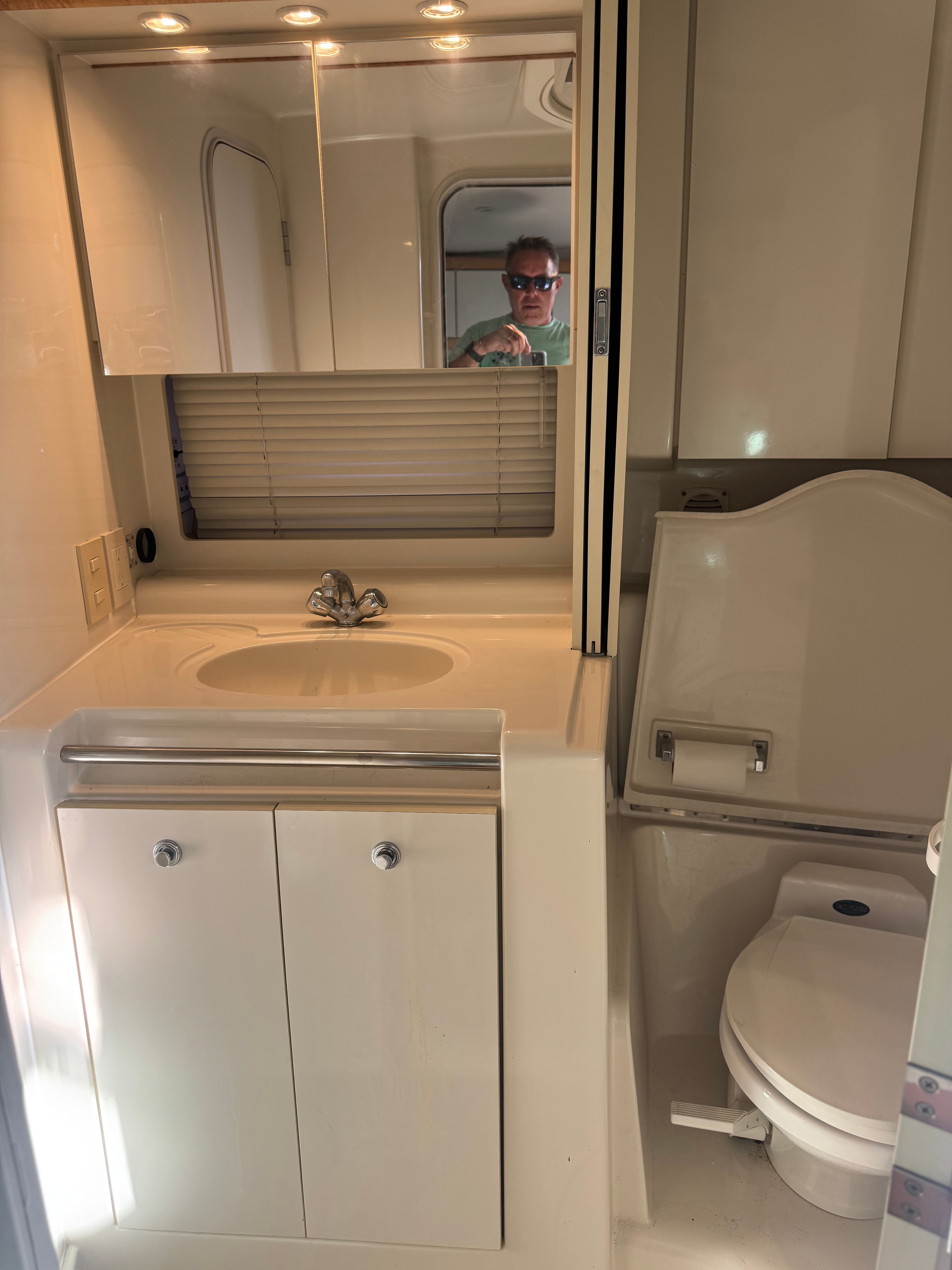 Bathroom in a boat with sink, mirror, and toilet. Bright lighting and compact layout.