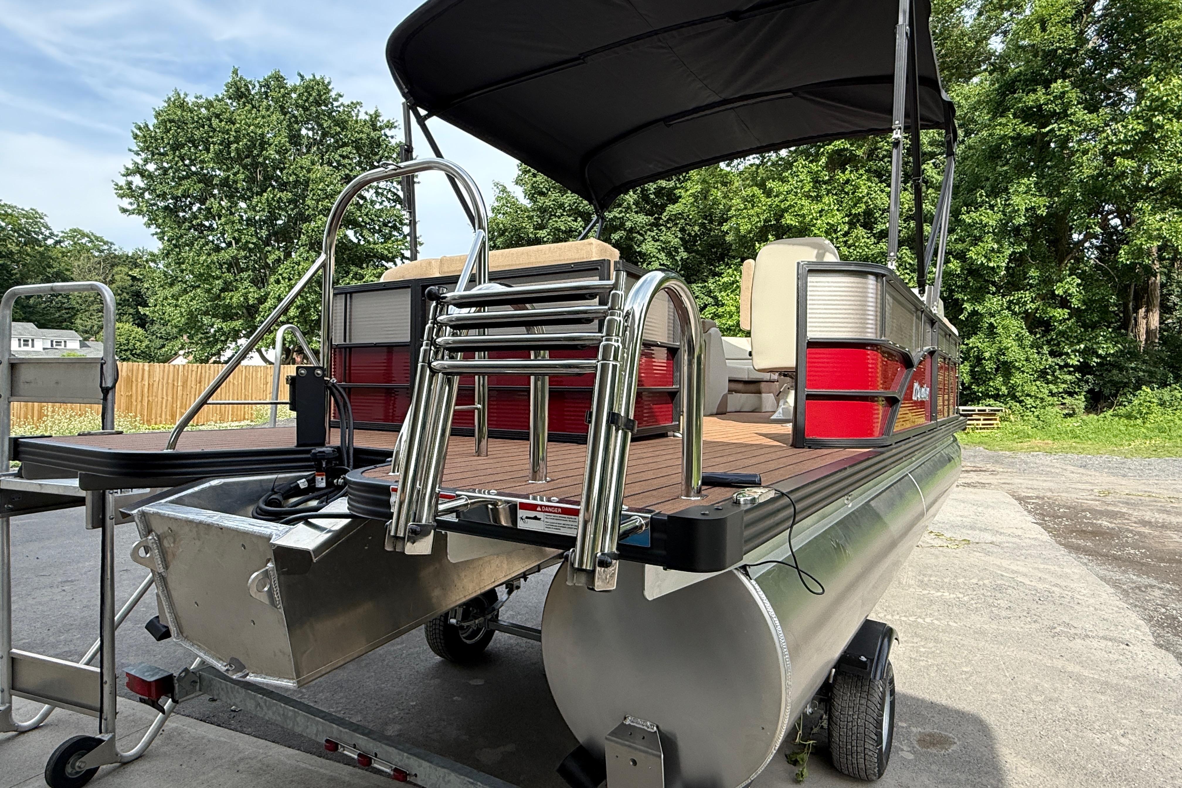 2027 Manitou 21 Aurora LE pontoon boat with canopy and ladder, parked outdoors.
