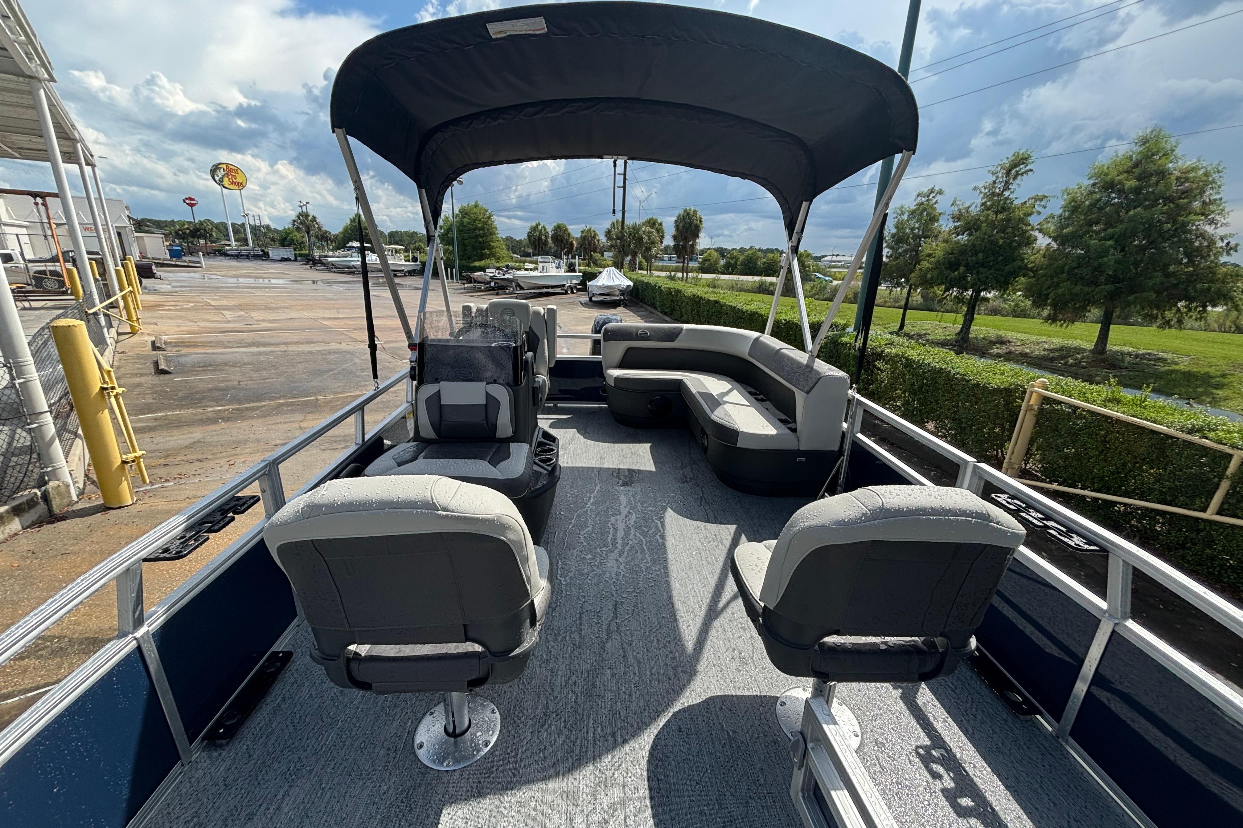 2026 Sun Tracker Bass Buggy 16 XL Select pontoon boat with seating and canopy, parked outdoors.