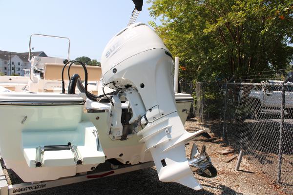 2023 Sundance DX20 boat with outboard motor, parked near a fence.