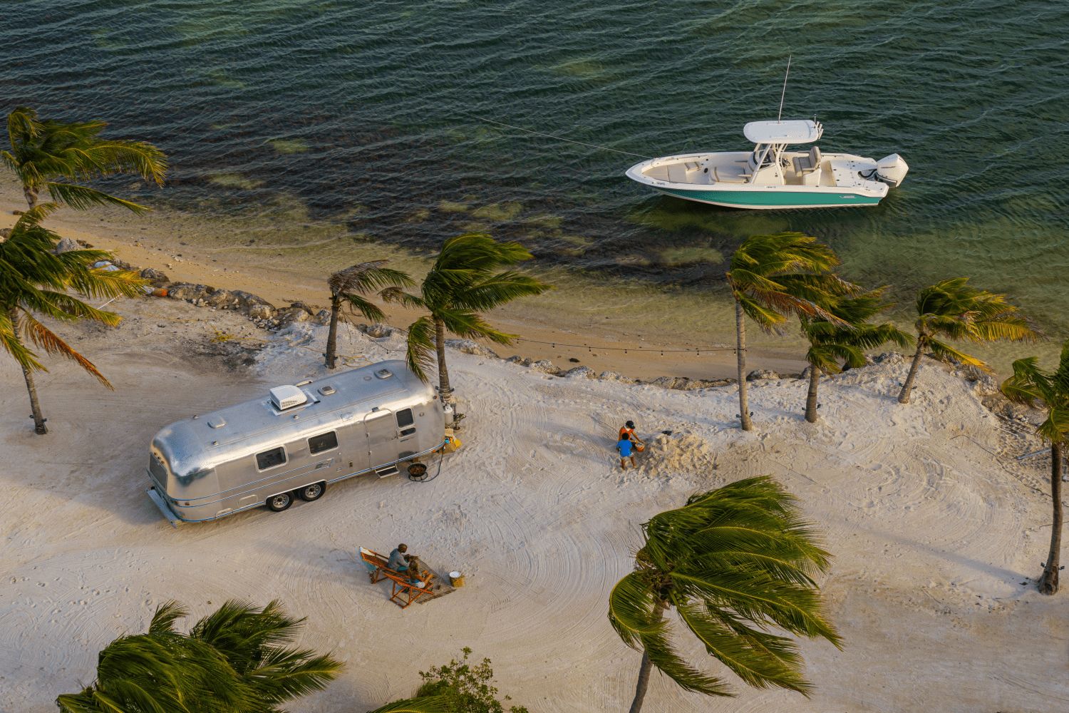 A Boston Whaler 25DA boat is anchored near a sandy beach with palm trees.