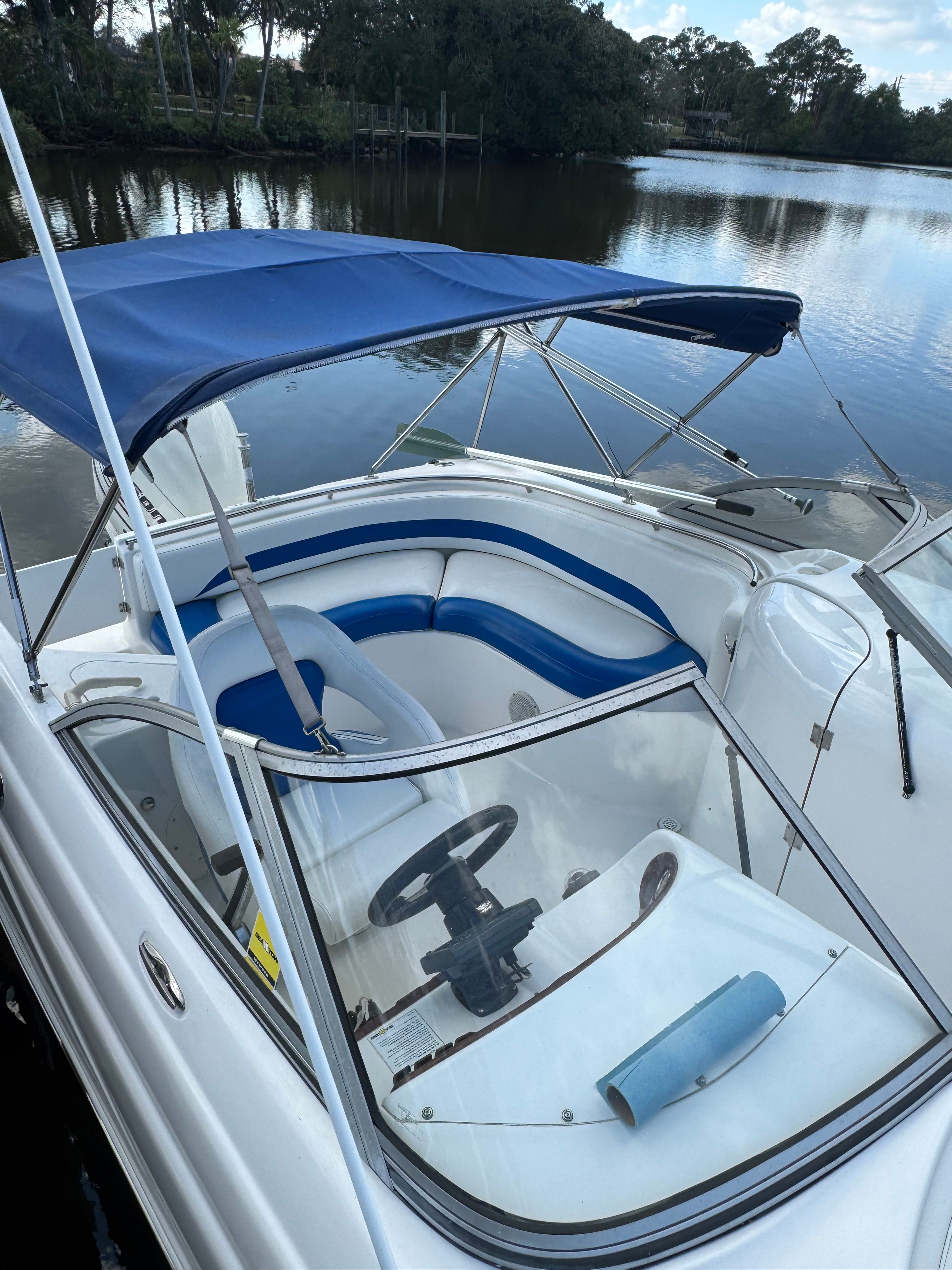 Boat with blue canopy and seating, docked by a calm waterway.