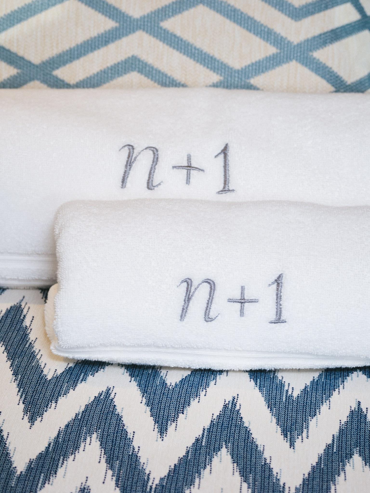 White towels with "n+1" embroidery on patterned blue background, Sunreef 70 Eco 2024.