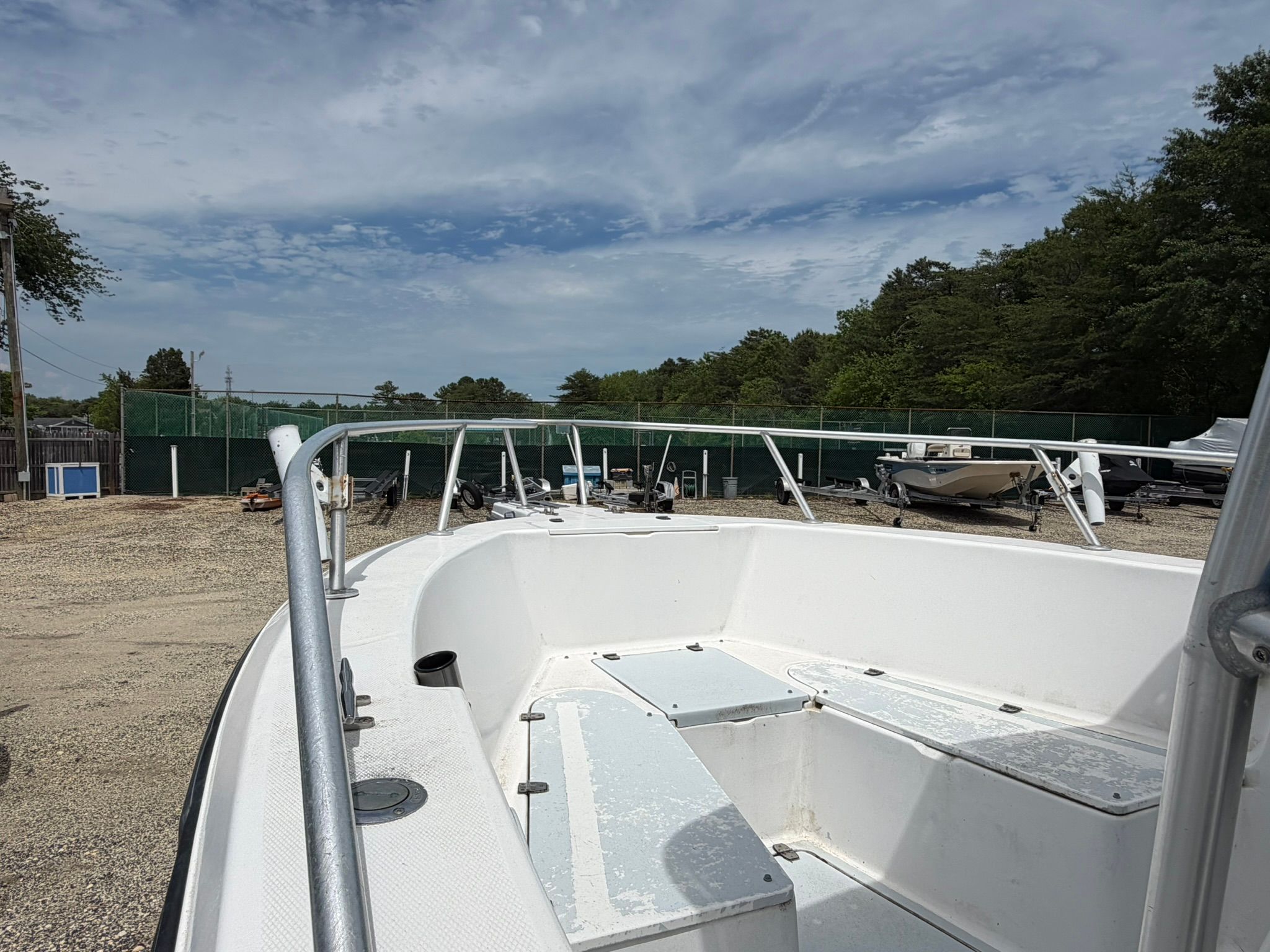 A white boat is on a dry dock, surrounded by trees and a fence.