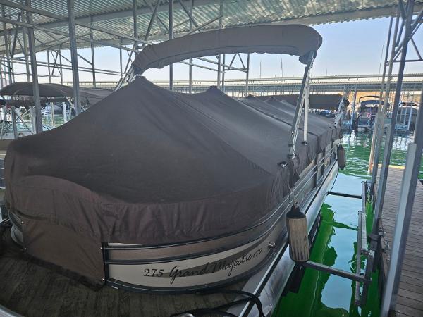 A covered pontoon boat is docked in a sheltered area. It has a brown cover.