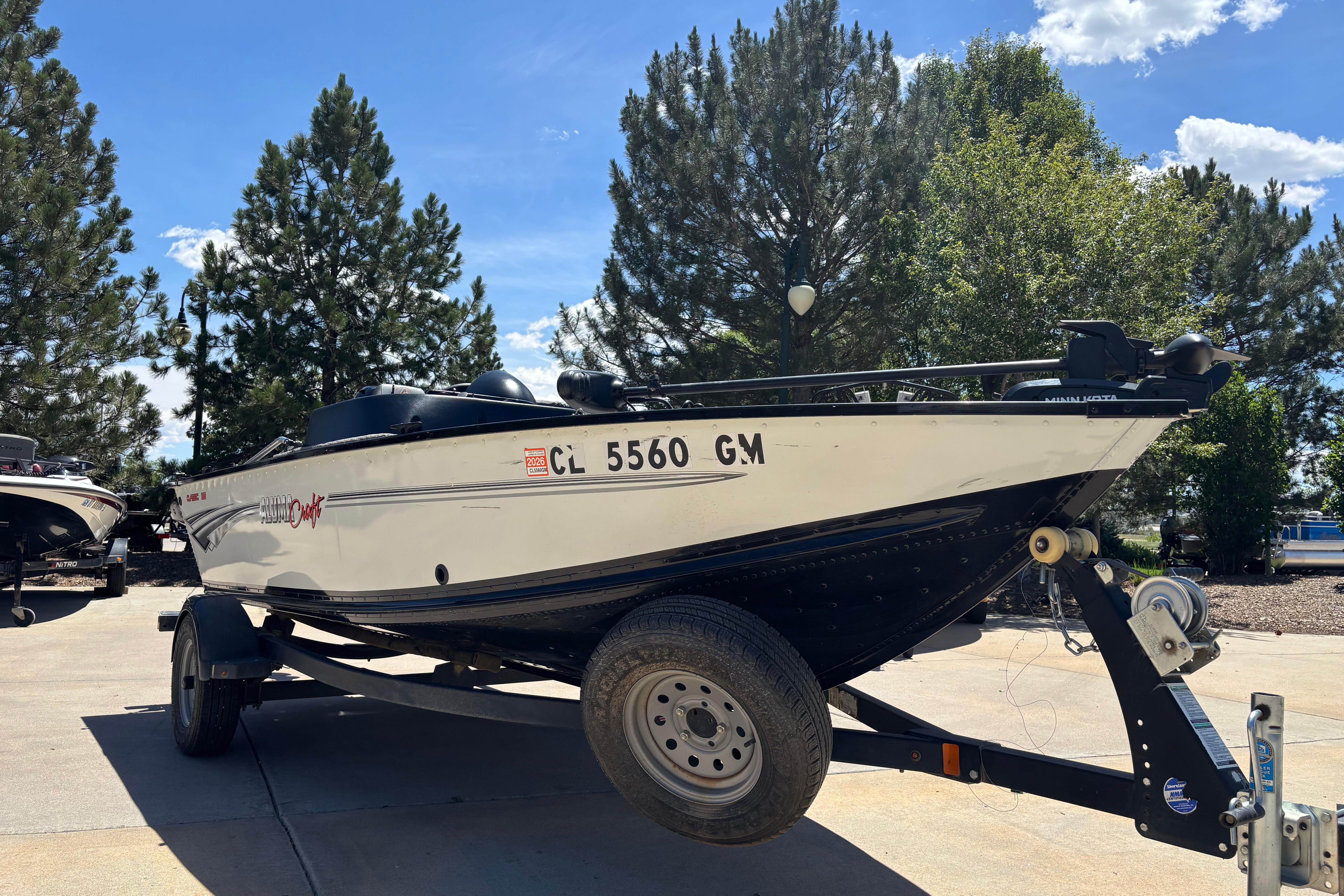2021 Alumacraft Classic 165 boat on trailer, parked outdoors with trees in background.