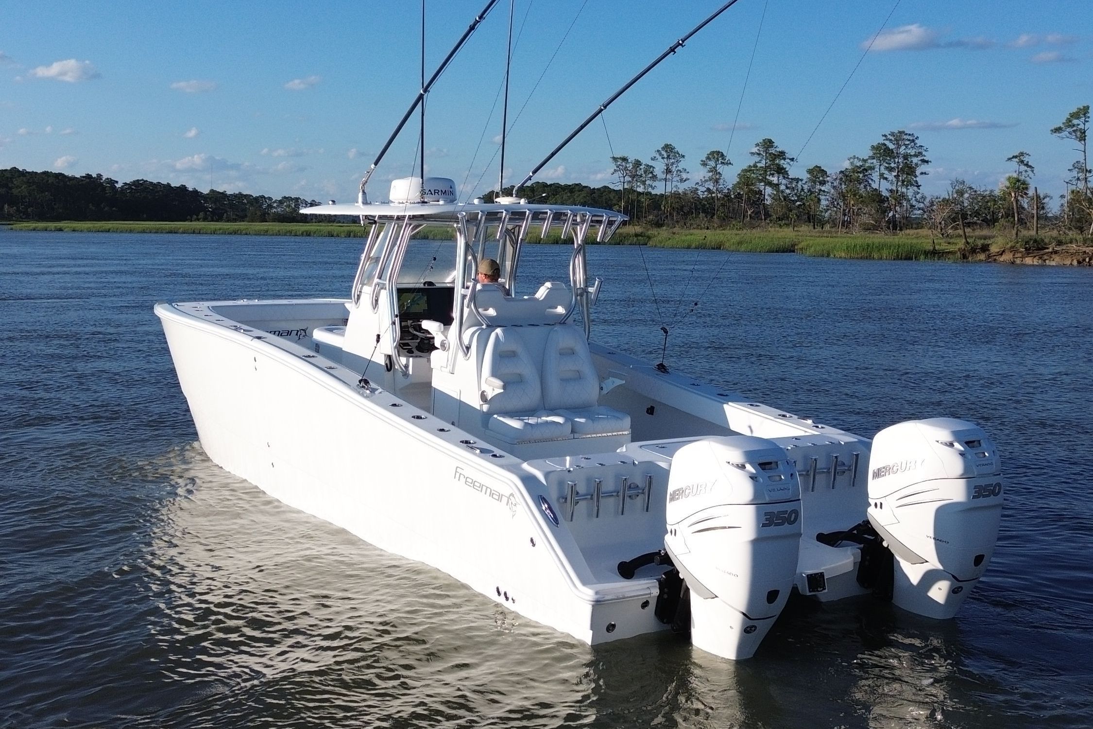 A white boat on calm water, featuring two outboard engines and fishing rods.