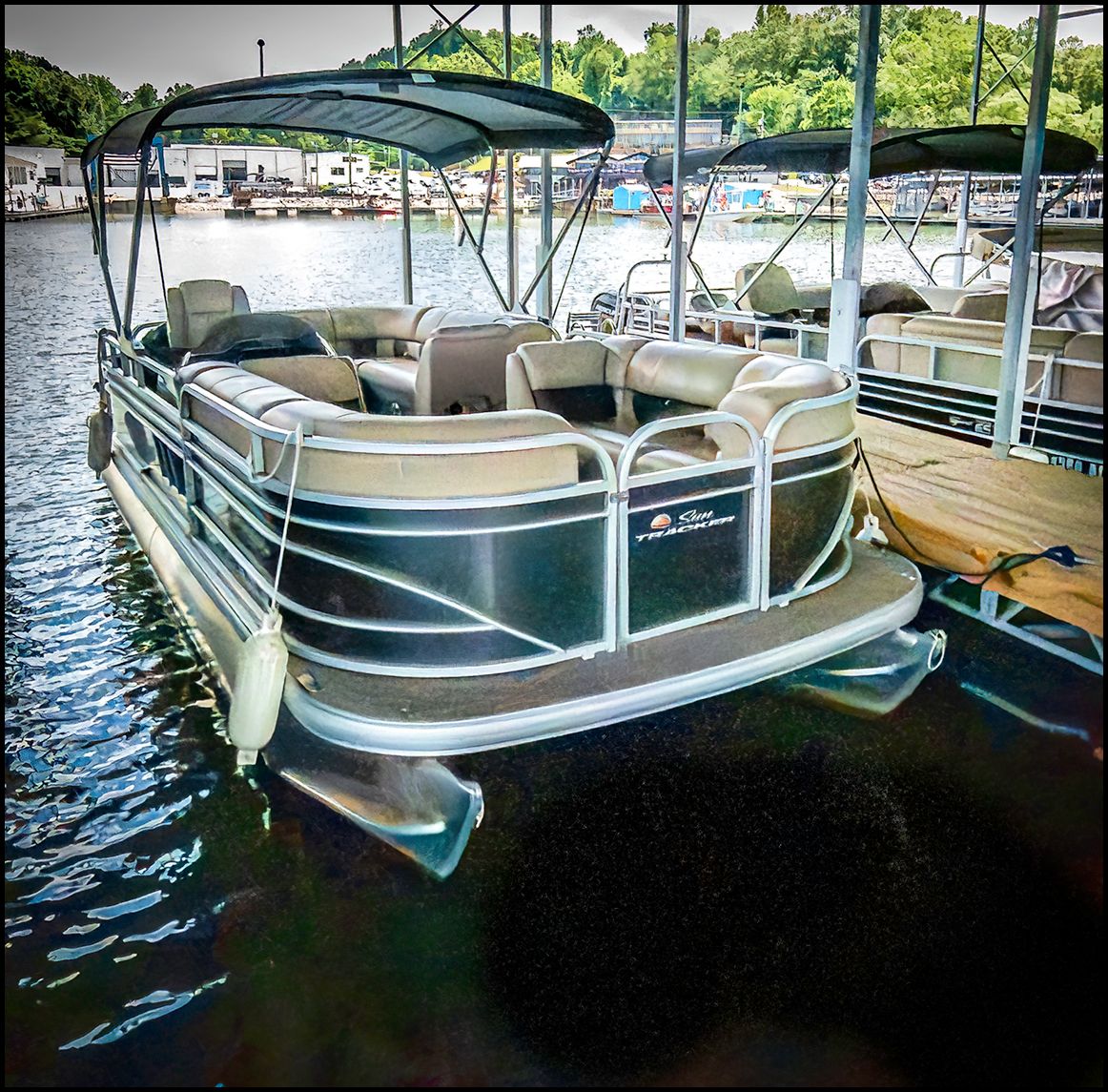 A Sun Tracker Party Barge 20 DLX pontoon boat docked. It features a canopy and comfortable seating.
