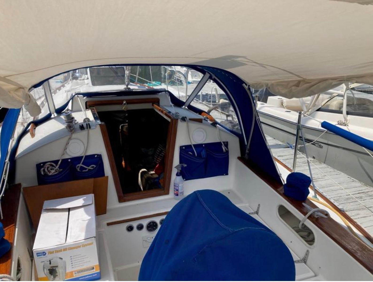 1982 Sabre 30 sailboat cockpit with blue canopy and marina background.