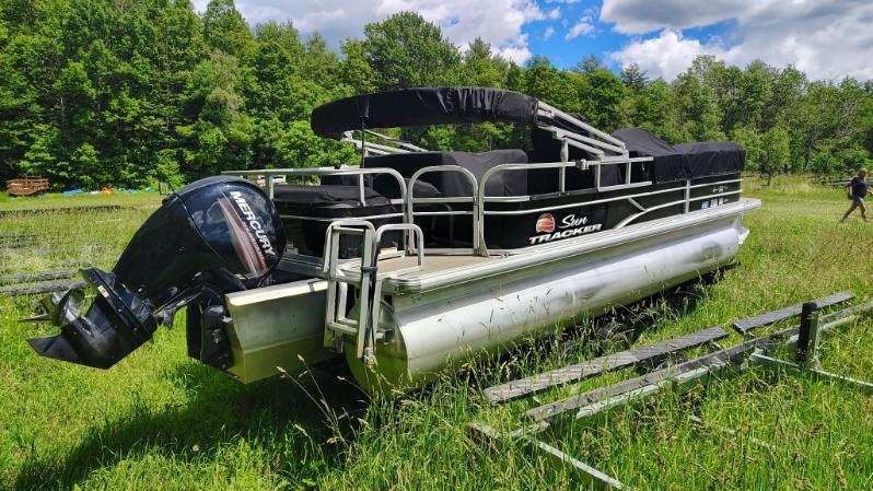 A 2019 White River sf22xp3 pb bk pontoon boat sits on grass in front of a forest.