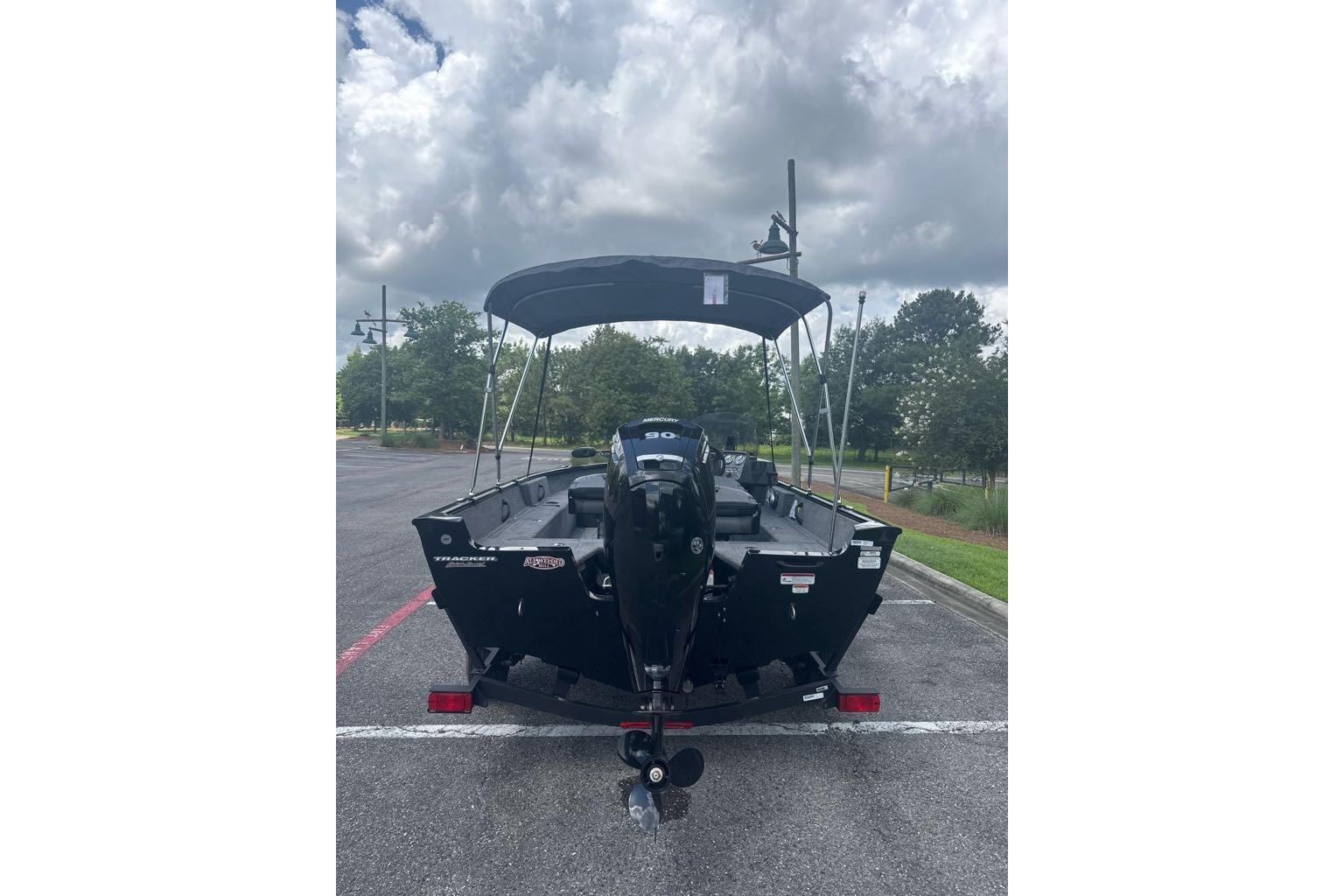 2026 Tracker Pro Guide V-16 SC boat with canopy, parked under cloudy sky.