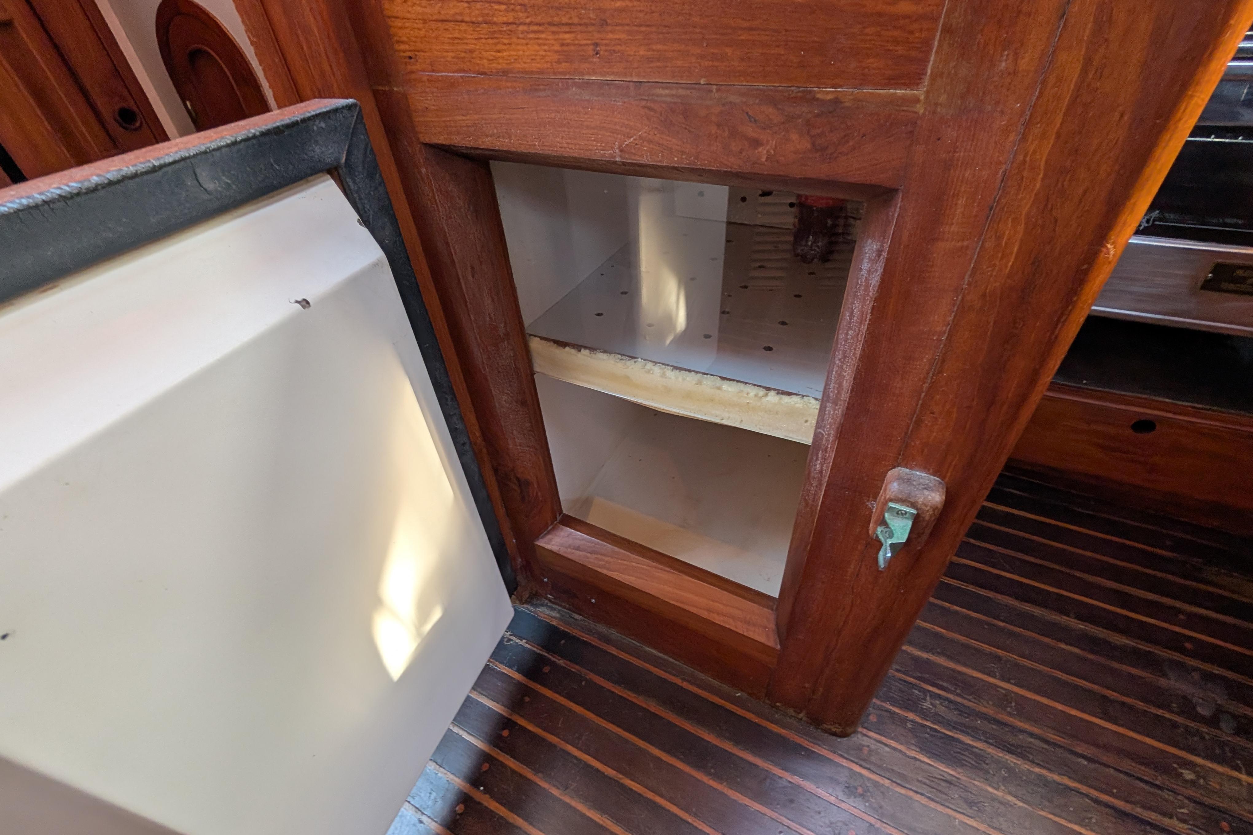 Wooden cabinet interior on a 1983 Robert Perry 41 boat, open door, empty shelves.