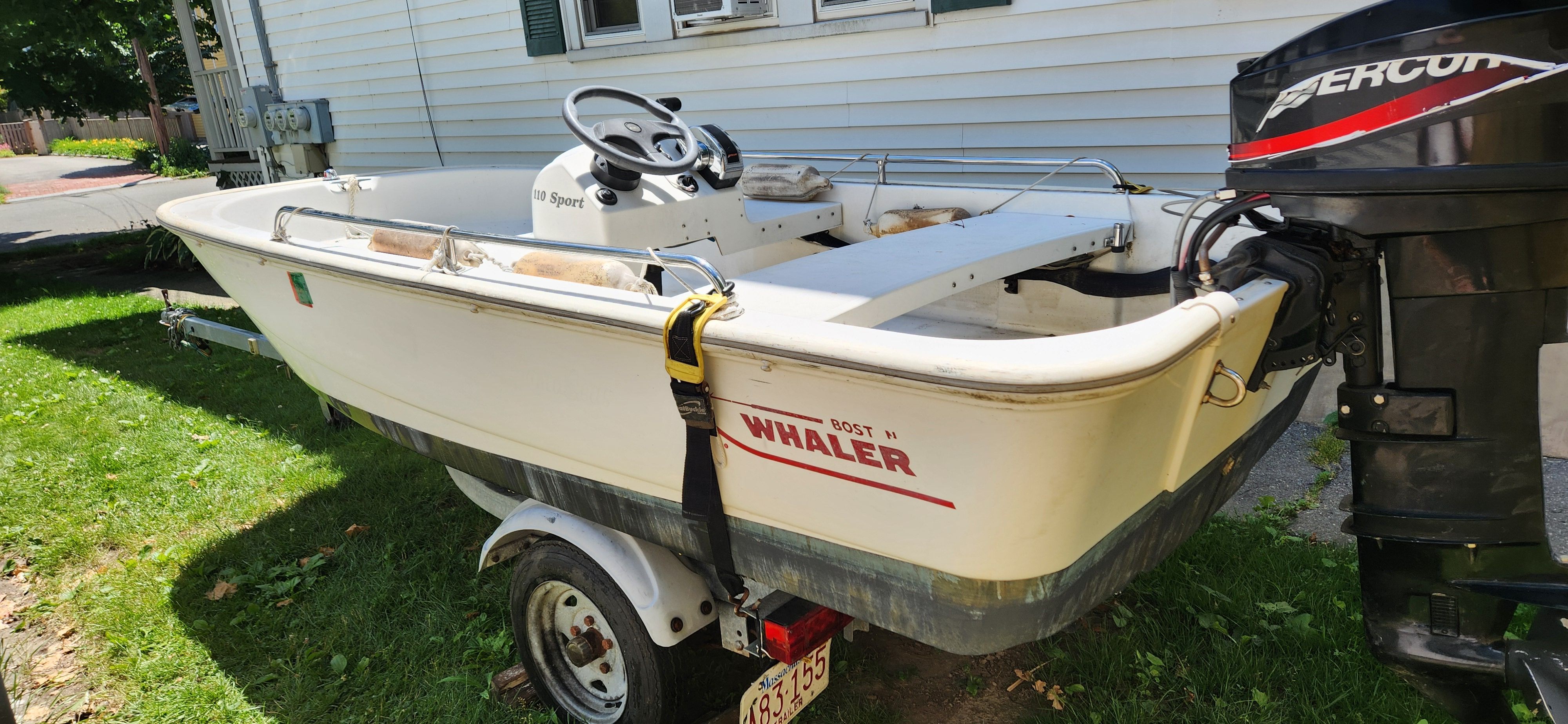 A Boston Whaler 110 Sport boat is on a trailer on grass.