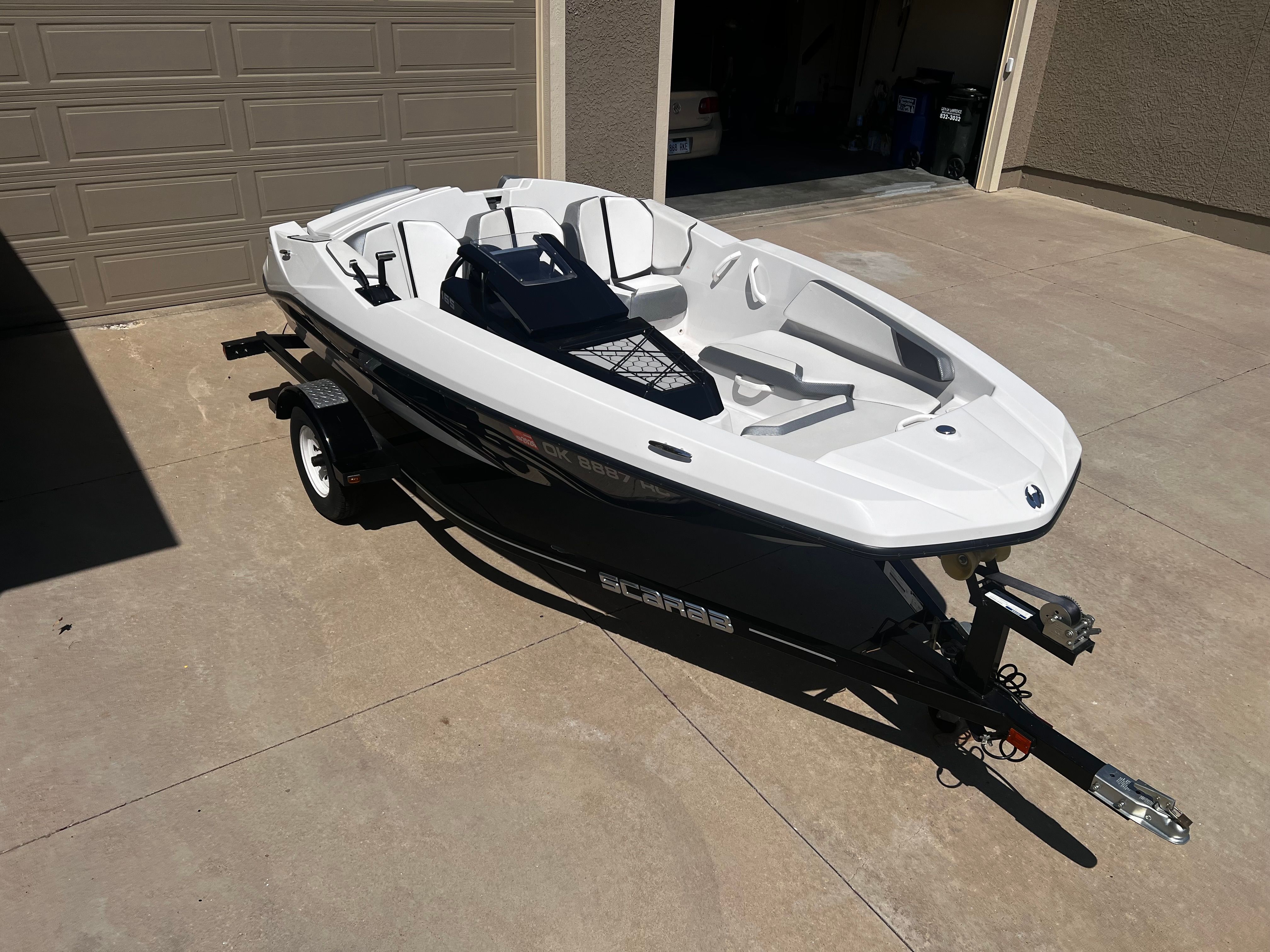 A white 2019 Scarab 165 G boat on a trailer in a driveway.