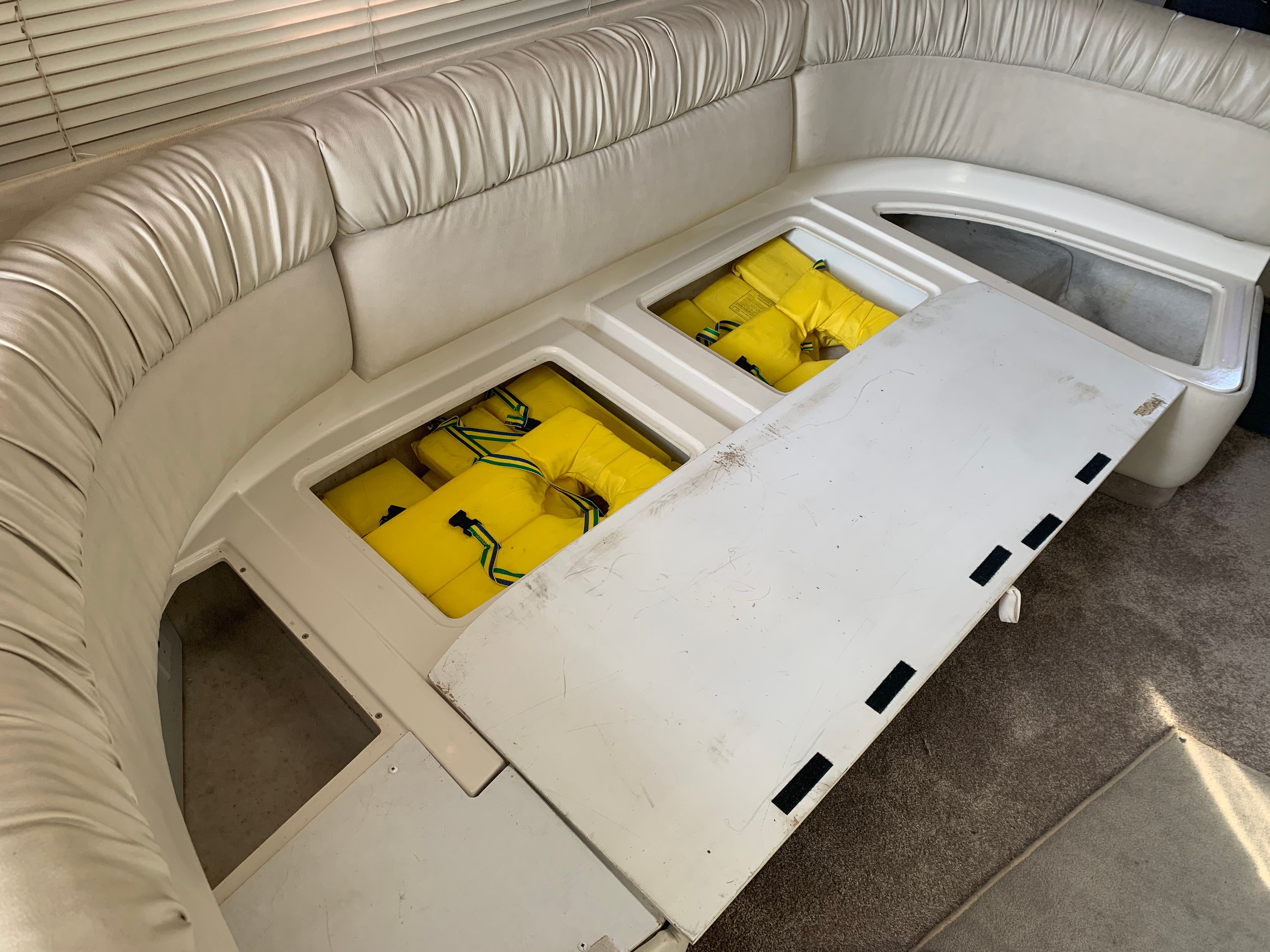 Boat interior with white cushioned seating and yellow life jackets stored in a compartment.