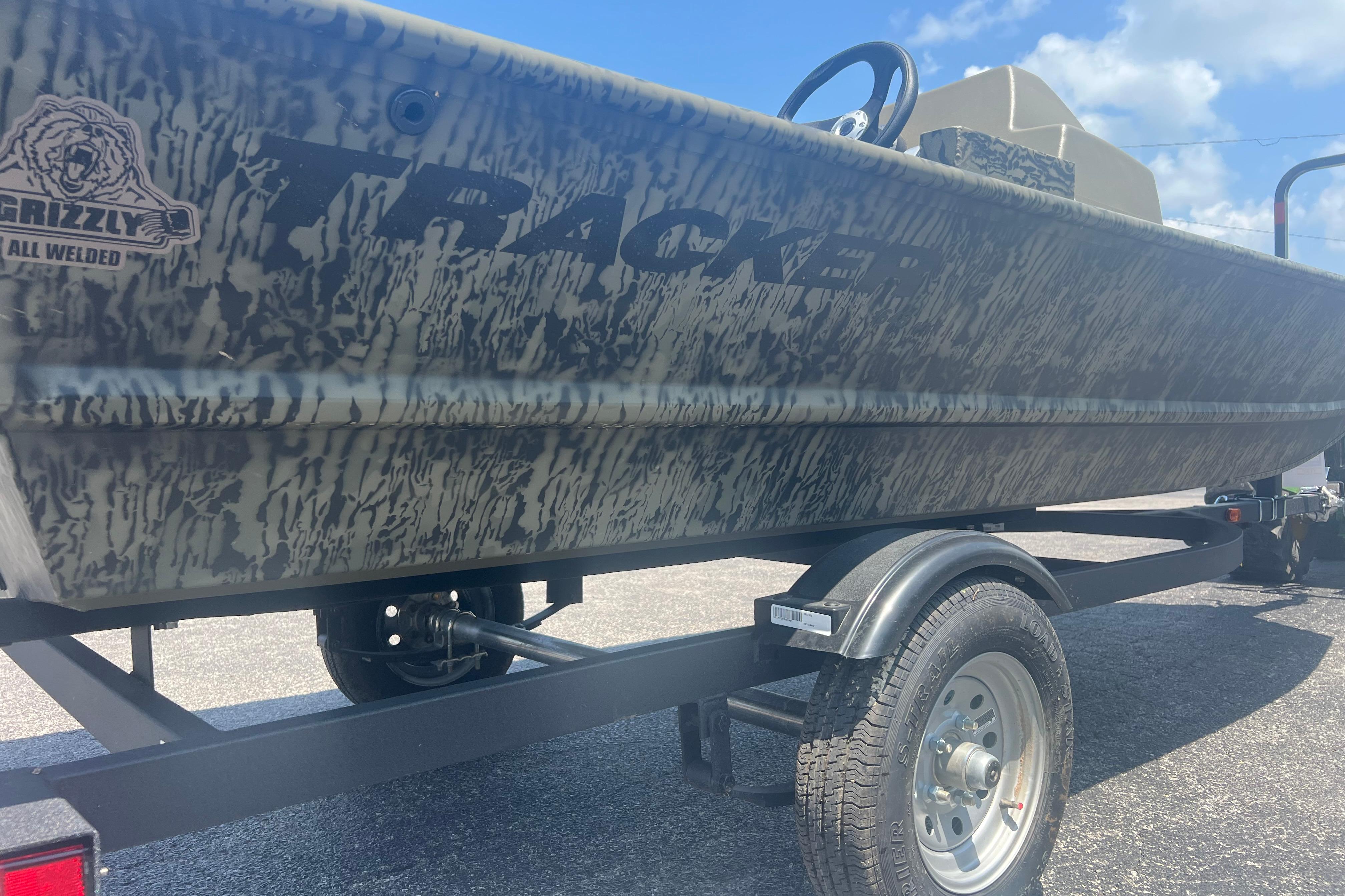 2026 Tracker Grizzly 1648 SC boat on trailer, featuring camouflage design under a blue sky.