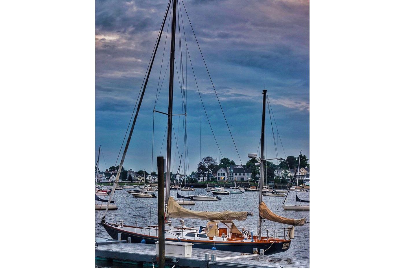 1970 Hinckley Bermuda 40 sailboat docked in a scenic harbor under a cloudy sky.