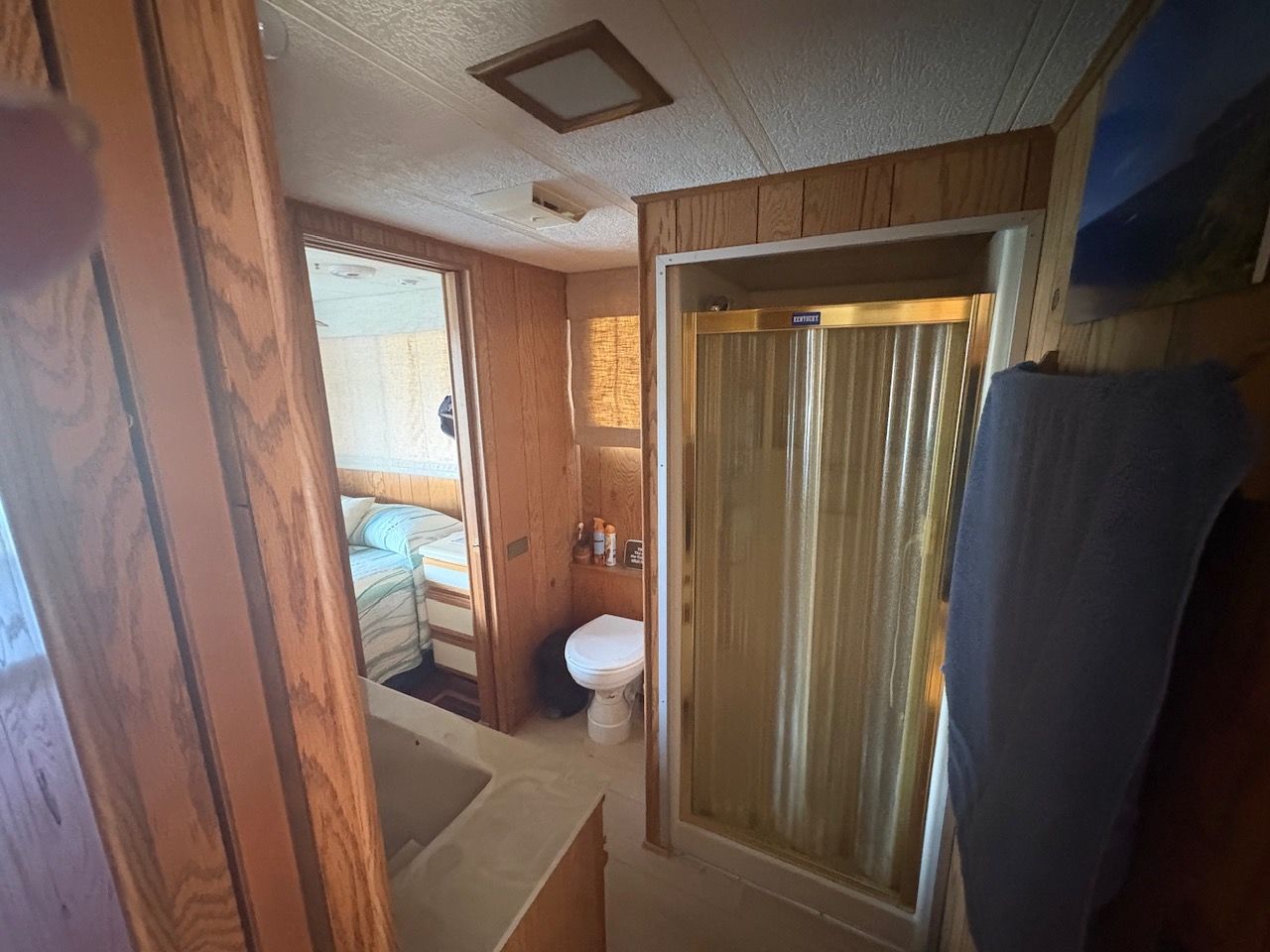 Interior of a houseboat with shower, sink, and toilet. Wood paneling and a bedroom in the background.