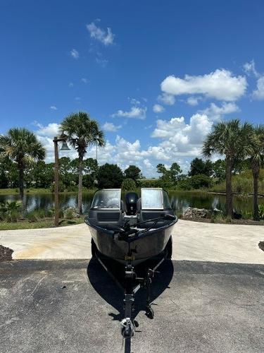 2025 Bass Tracker PGV16WT boat on trailer, parked near scenic lake with palm trees.