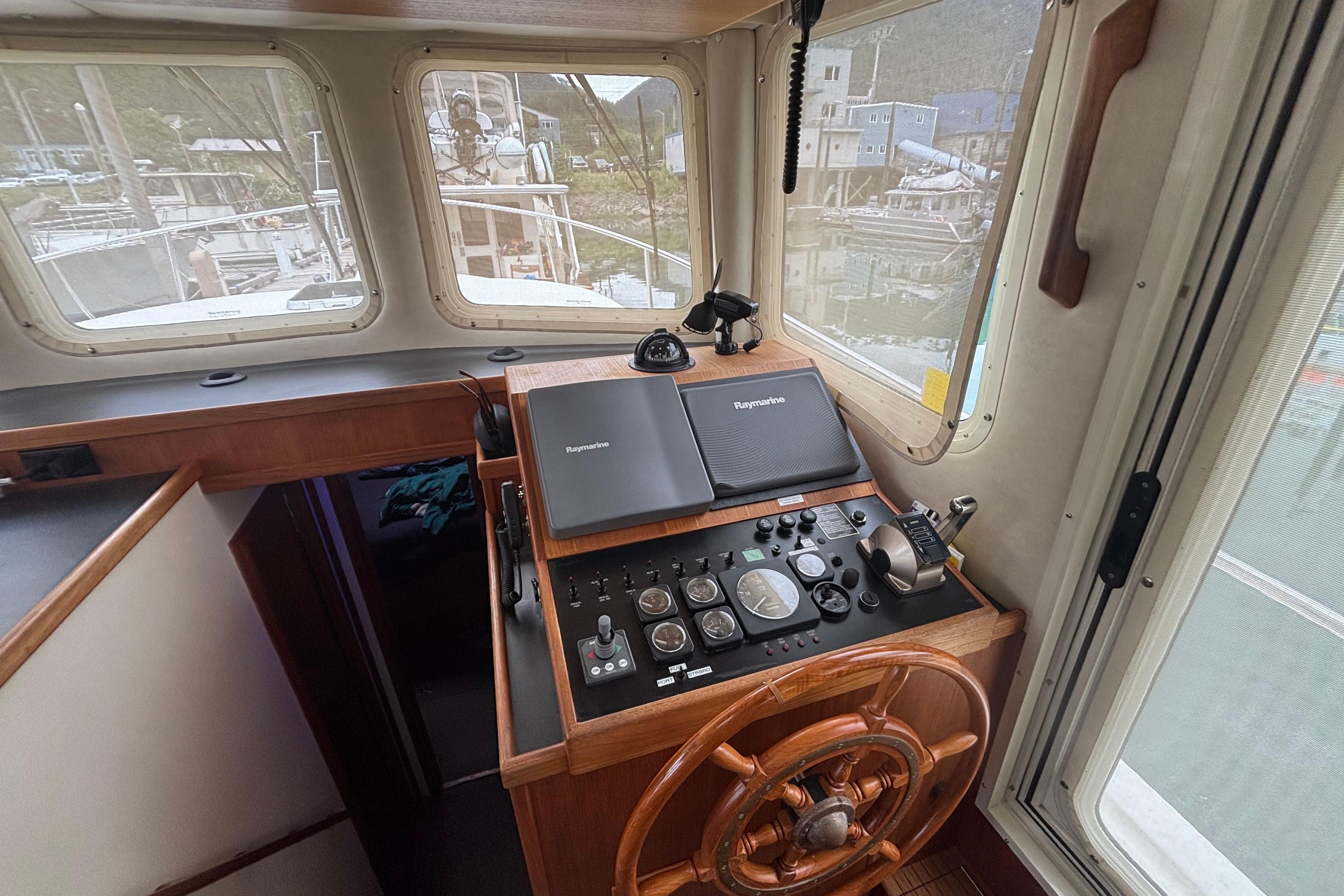 Pilothouse of 2004 Nordic Tug 37 with navigation equipment and wooden steering wheel.