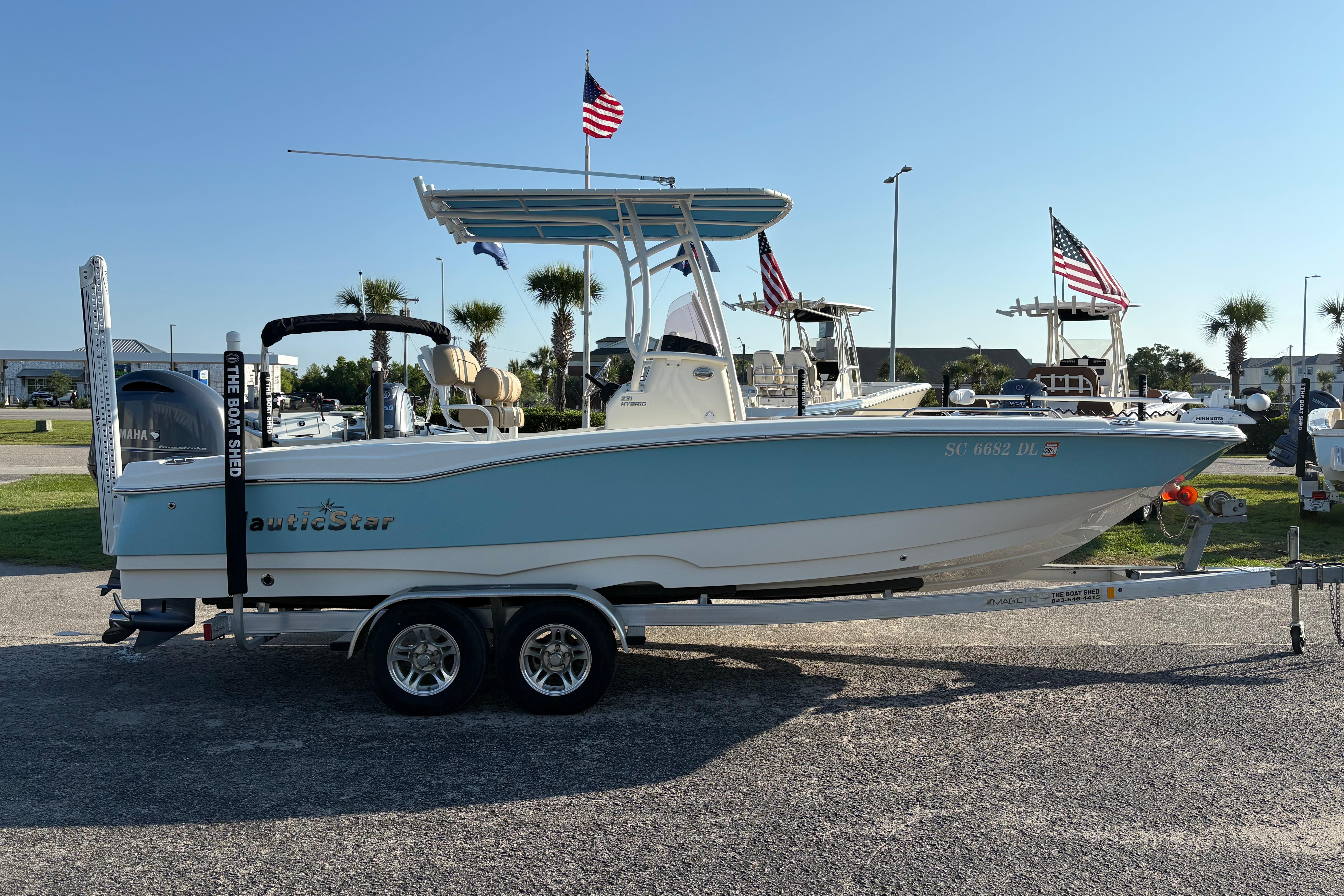 2019 NauticStar 231 Hybrid boat on trailer, displayed outdoors with flags.