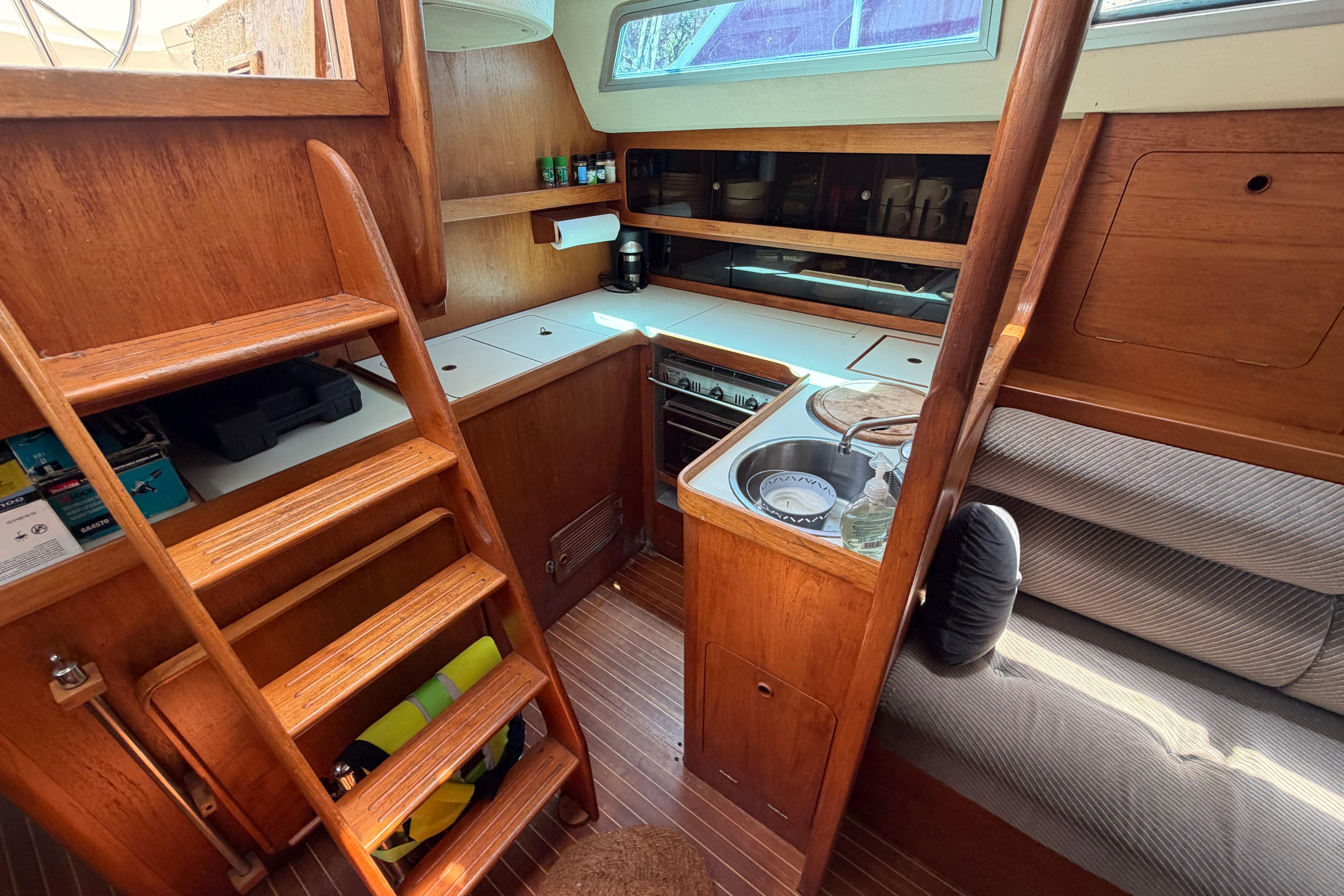 Cozy 1987 Moody 376 yacht interior with wooden cabinetry, compact kitchen, and seating area.