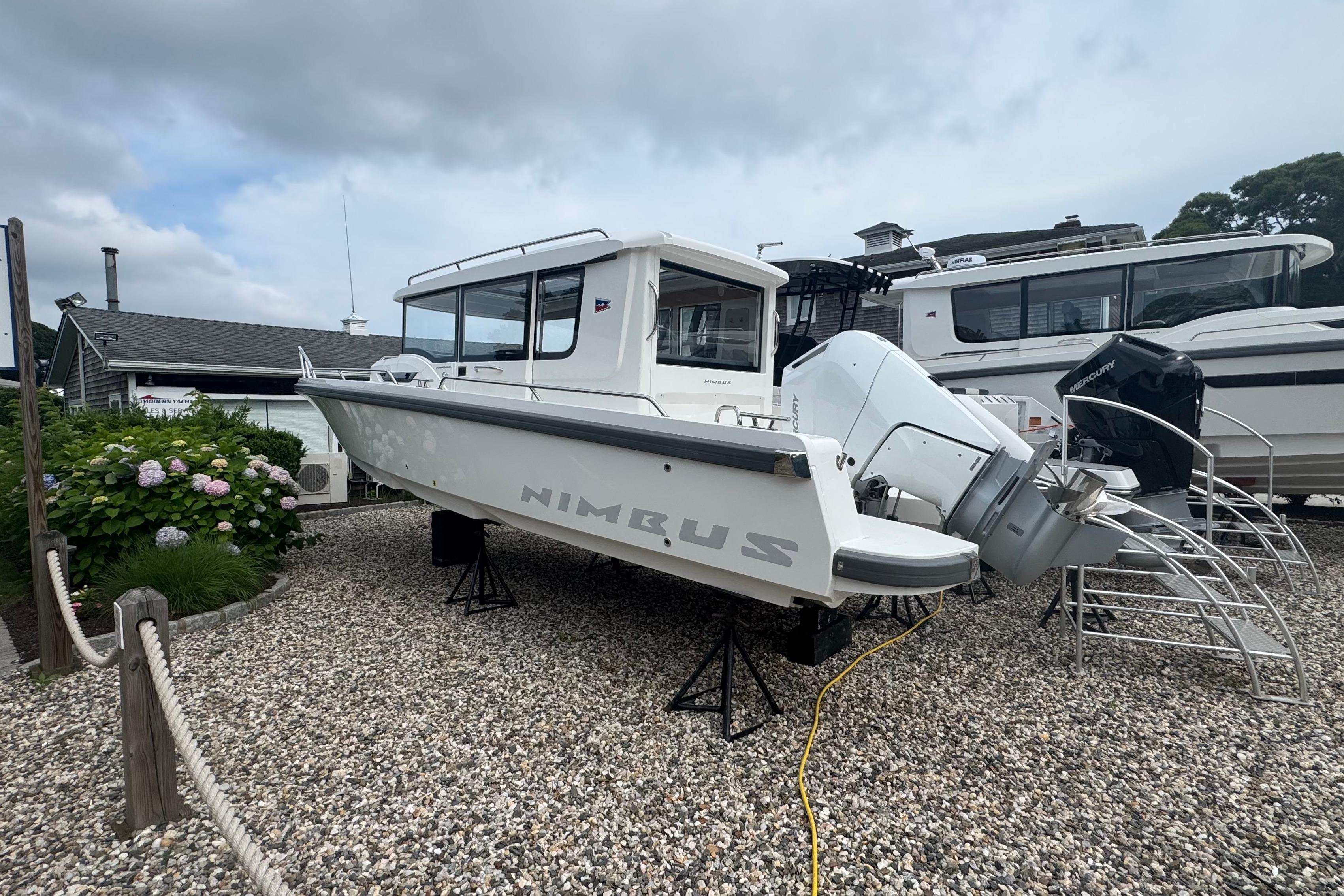 Nimbus Commuter 9 from 2026 on a gravel lot, with outboard engines and surrounding boats.