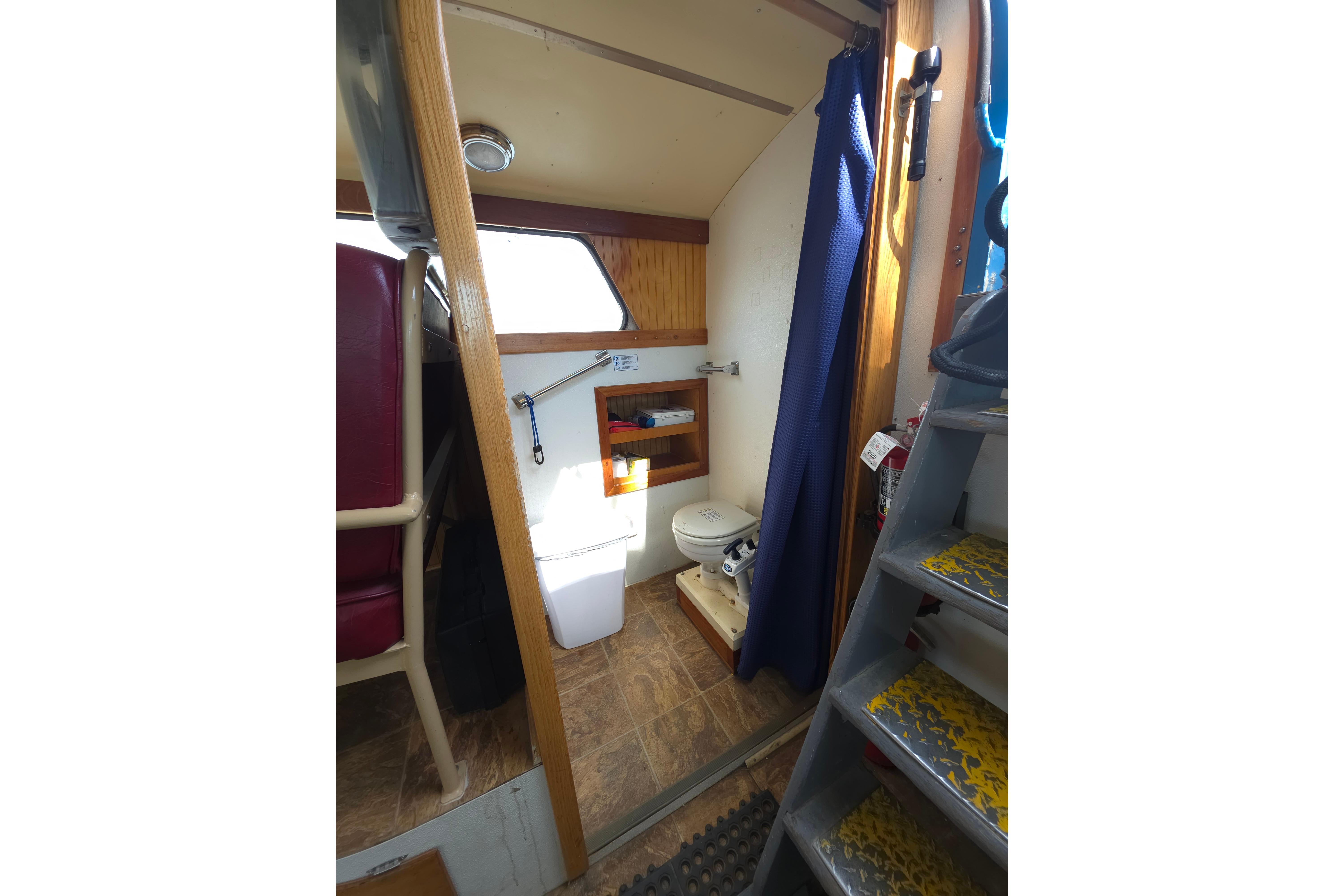 Interior of 1974 Breaux's Bay Craft boat, featuring a compact bathroom with toilet and curtain.
