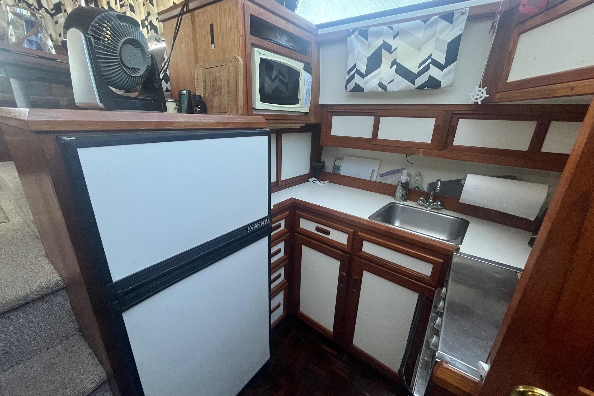Compact kitchen in 1990 Cooper Prowler 35 boat with fridge, sink, and microwave.