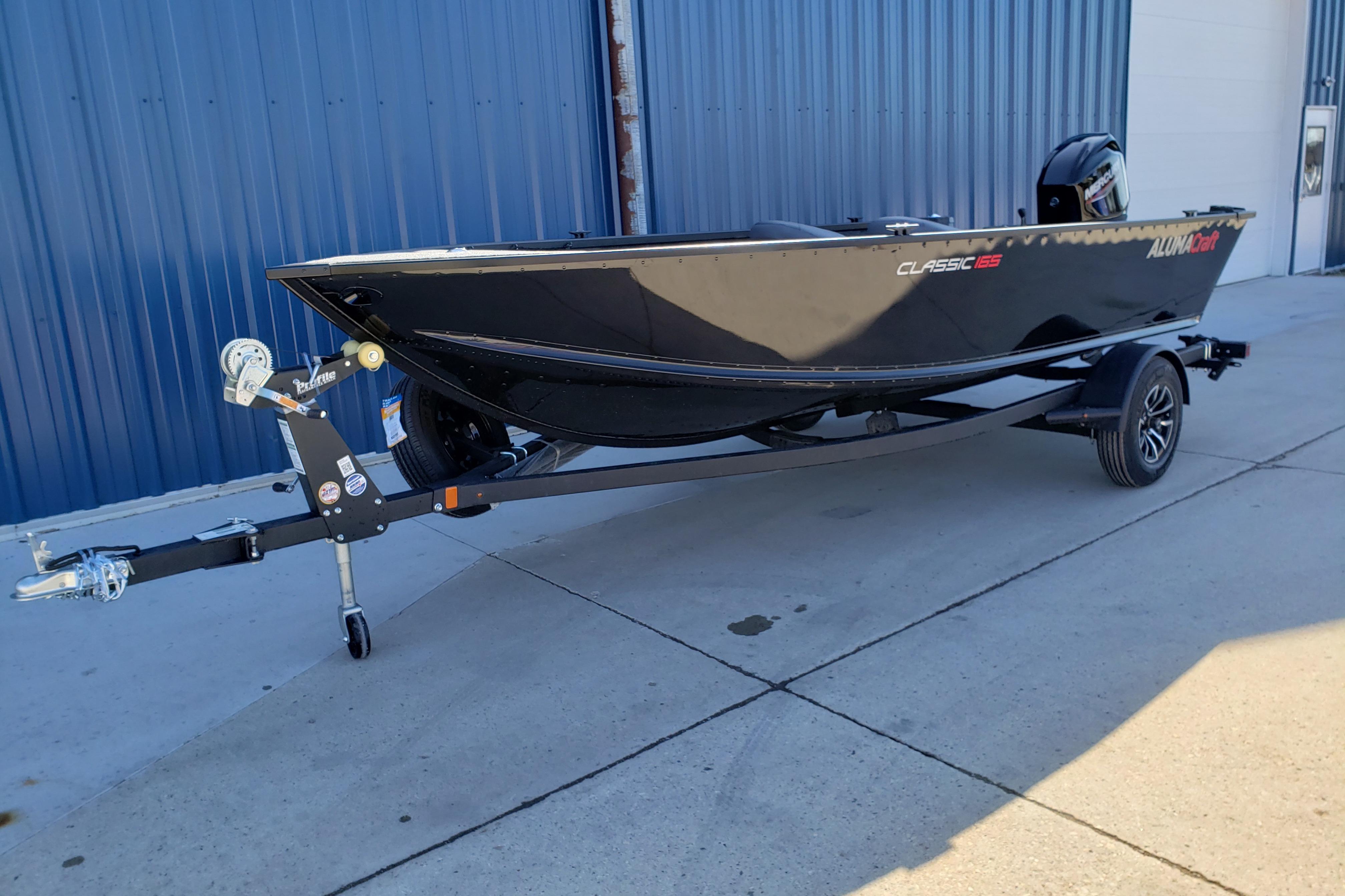 2026 Alumacraft Classic 165 Tiller boat on trailer, parked outdoors.