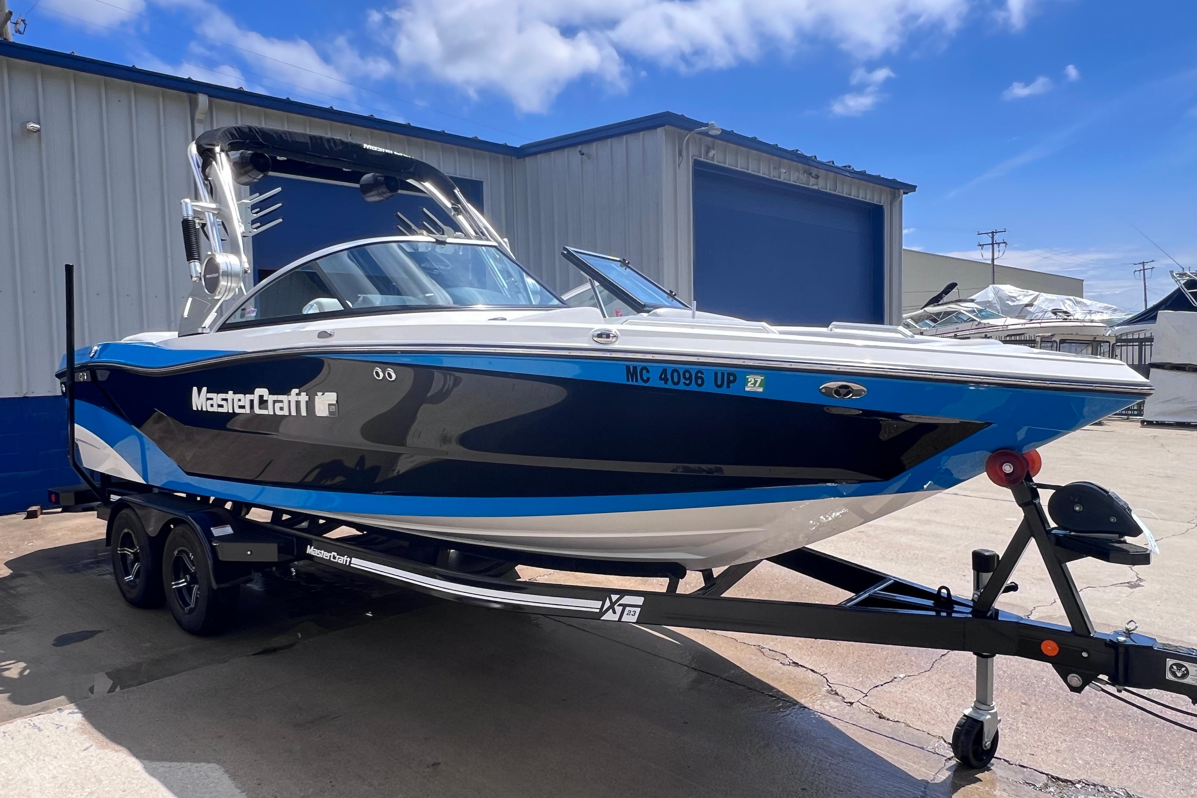 2021 MasterCraft XT23 boat on trailer, parked outside a warehouse under a blue sky.