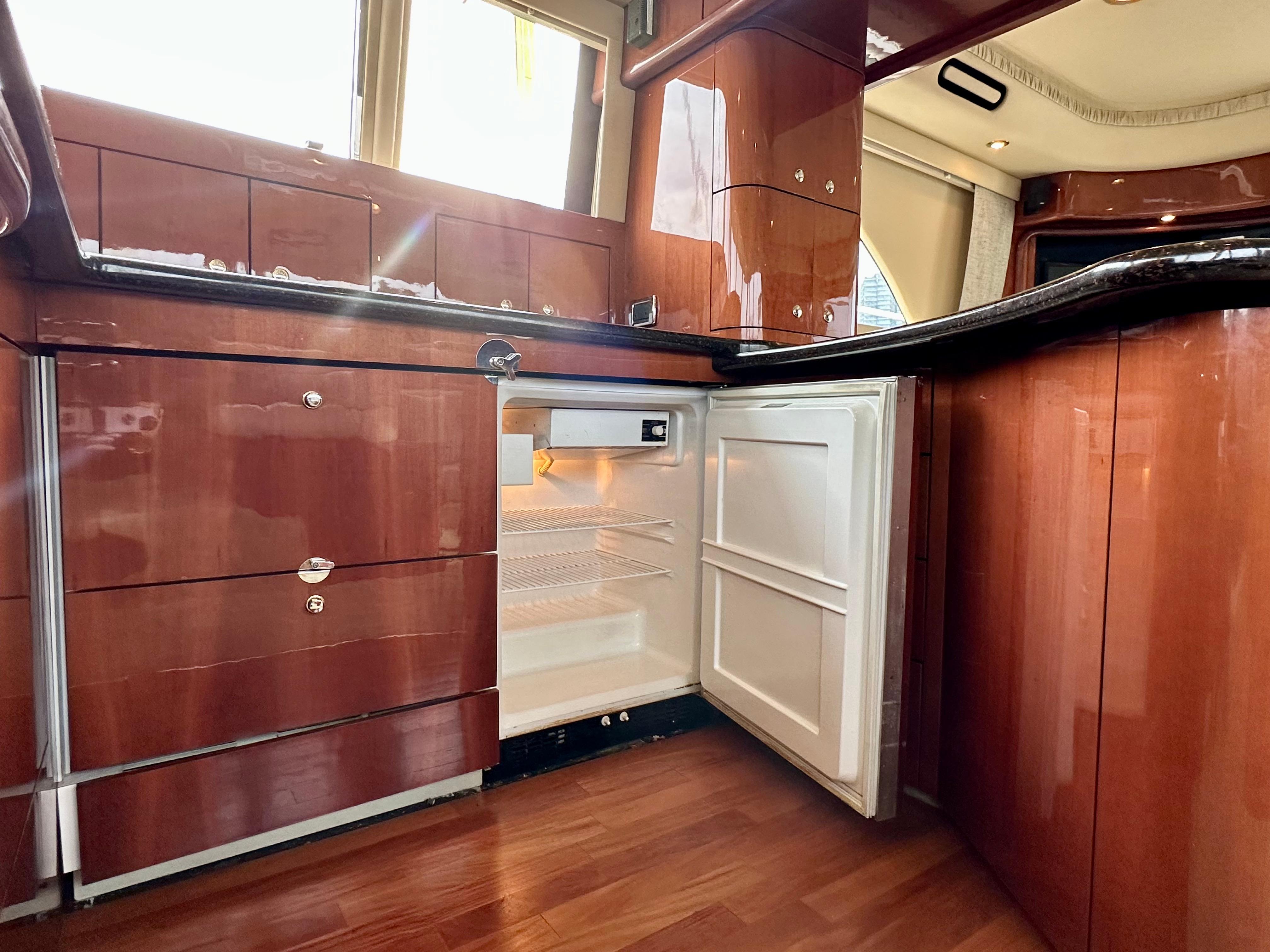 Interior of 2002 Sea Ray 560 Sedan Bridge yacht, featuring open fridge and wooden cabinetry.