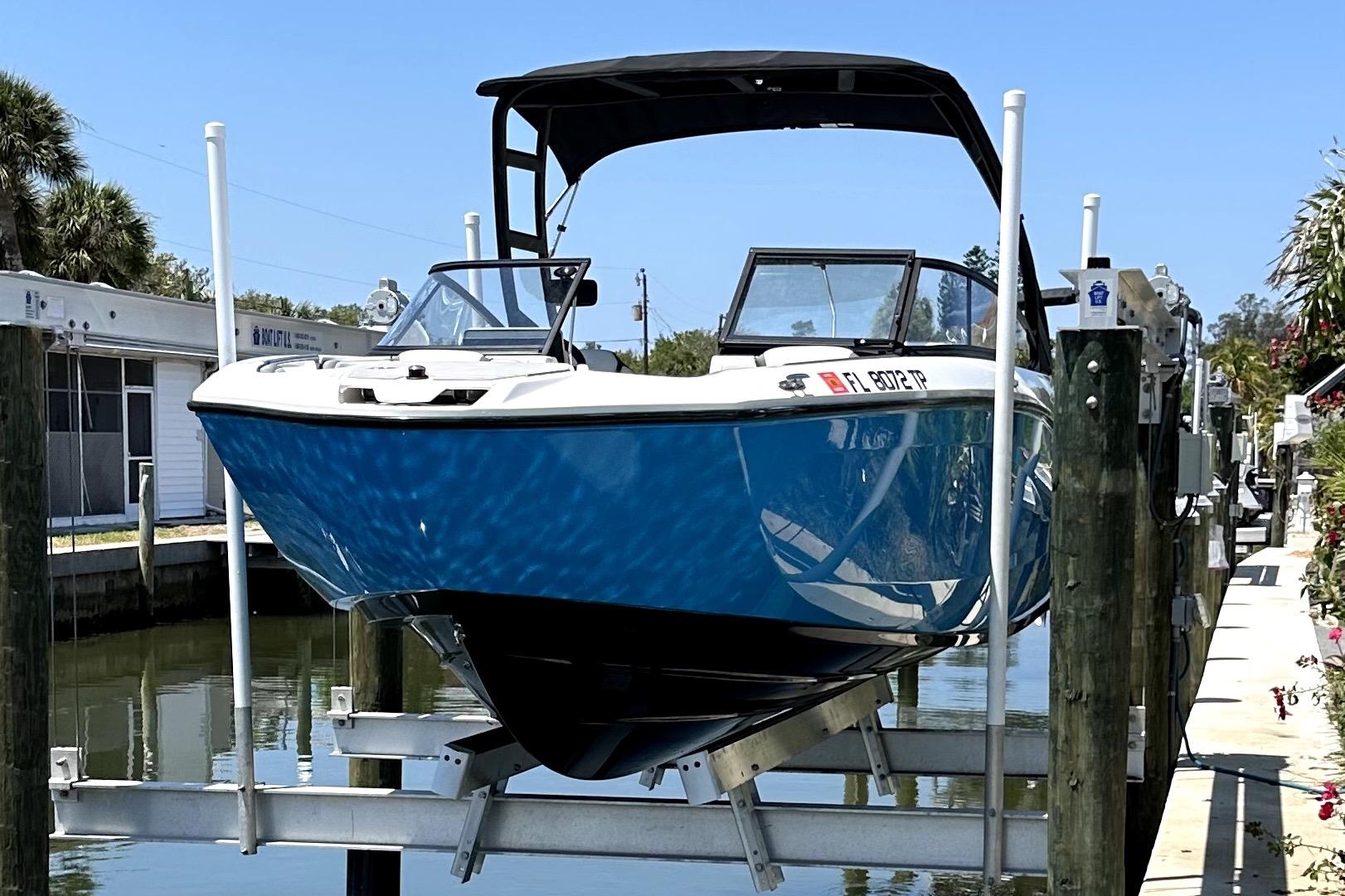 2023 Yamaha Boats AR250 on lift, blue hull, docked by canal.