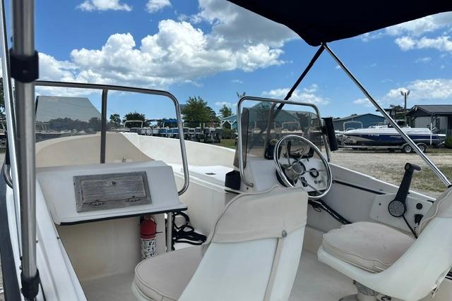 1989 Henry O 150 Dual Console boat interior with steering wheel and seating under blue sky.
