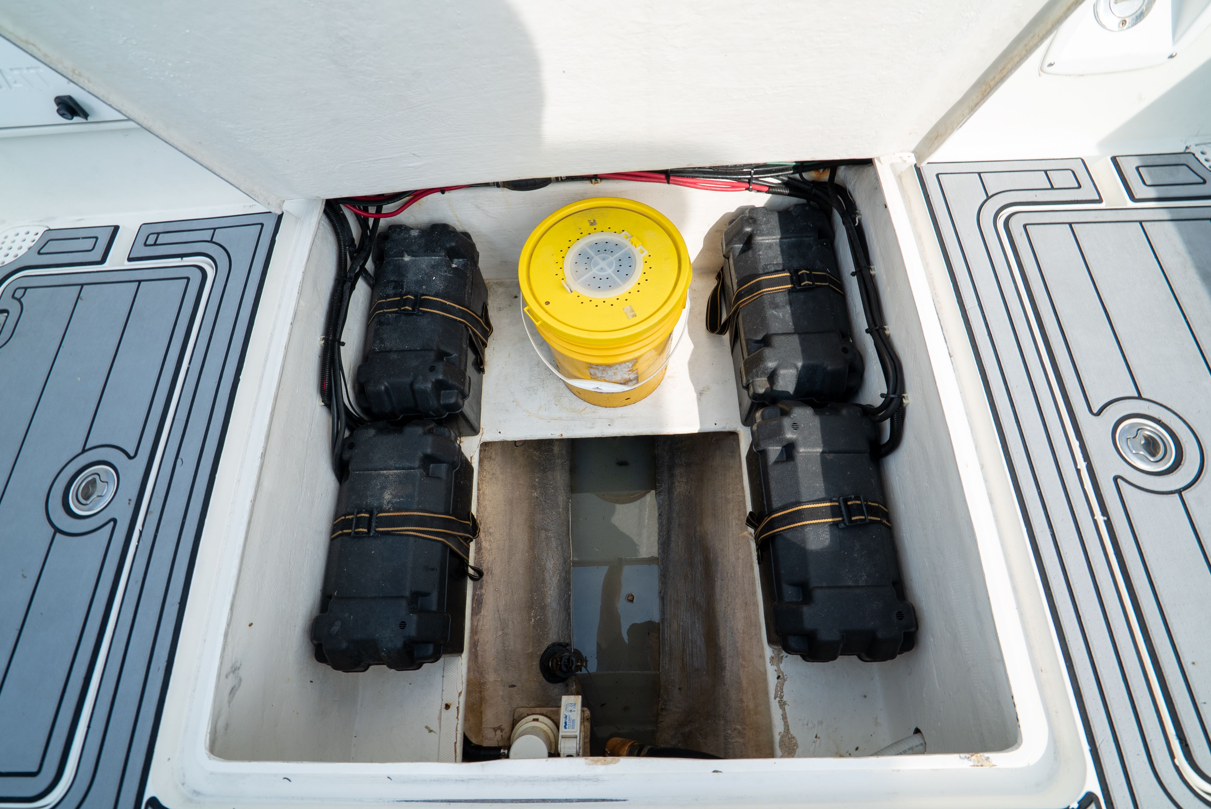 An open storage compartment on a boat with batteries and a yellow bucket.