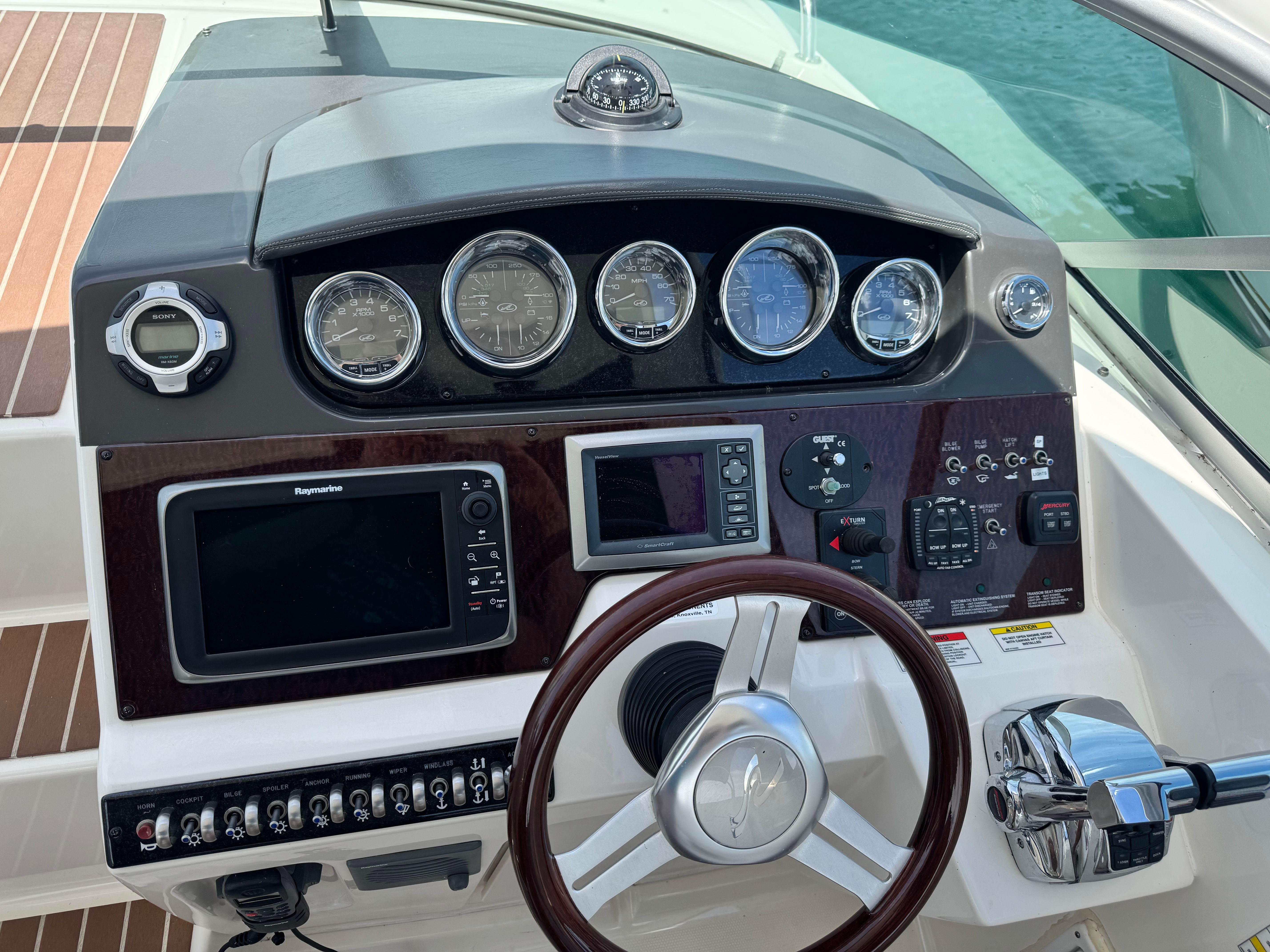 The dashboard of a 2010 Sea Ray Sundancer 310 with multiple gauges and a wooden steering wheel.