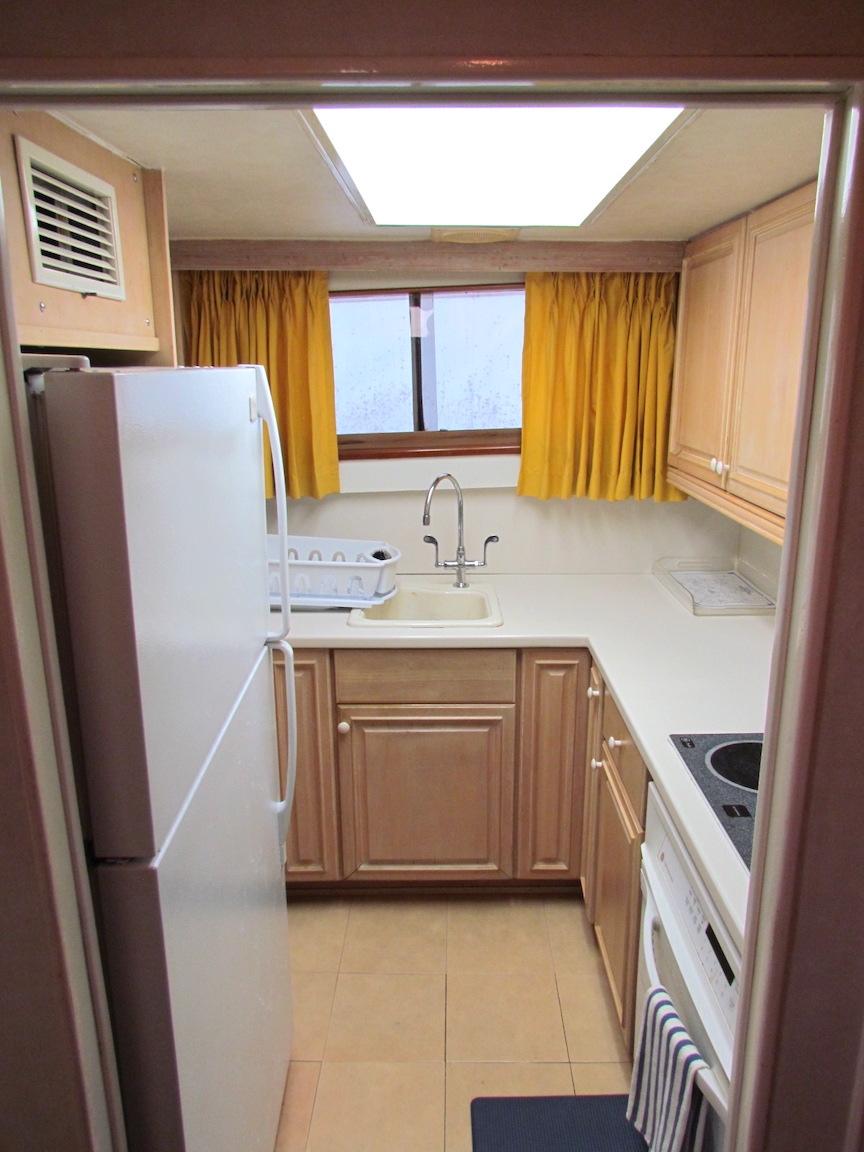1972 Hargrave 67 Motor Yacht kitchen with wooden cabinets and yellow curtains.
