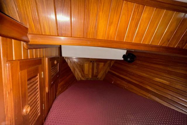 Interior cabin of 1986 Cabo Rico CB38 sailboat with wooden paneling and maroon bedding.
