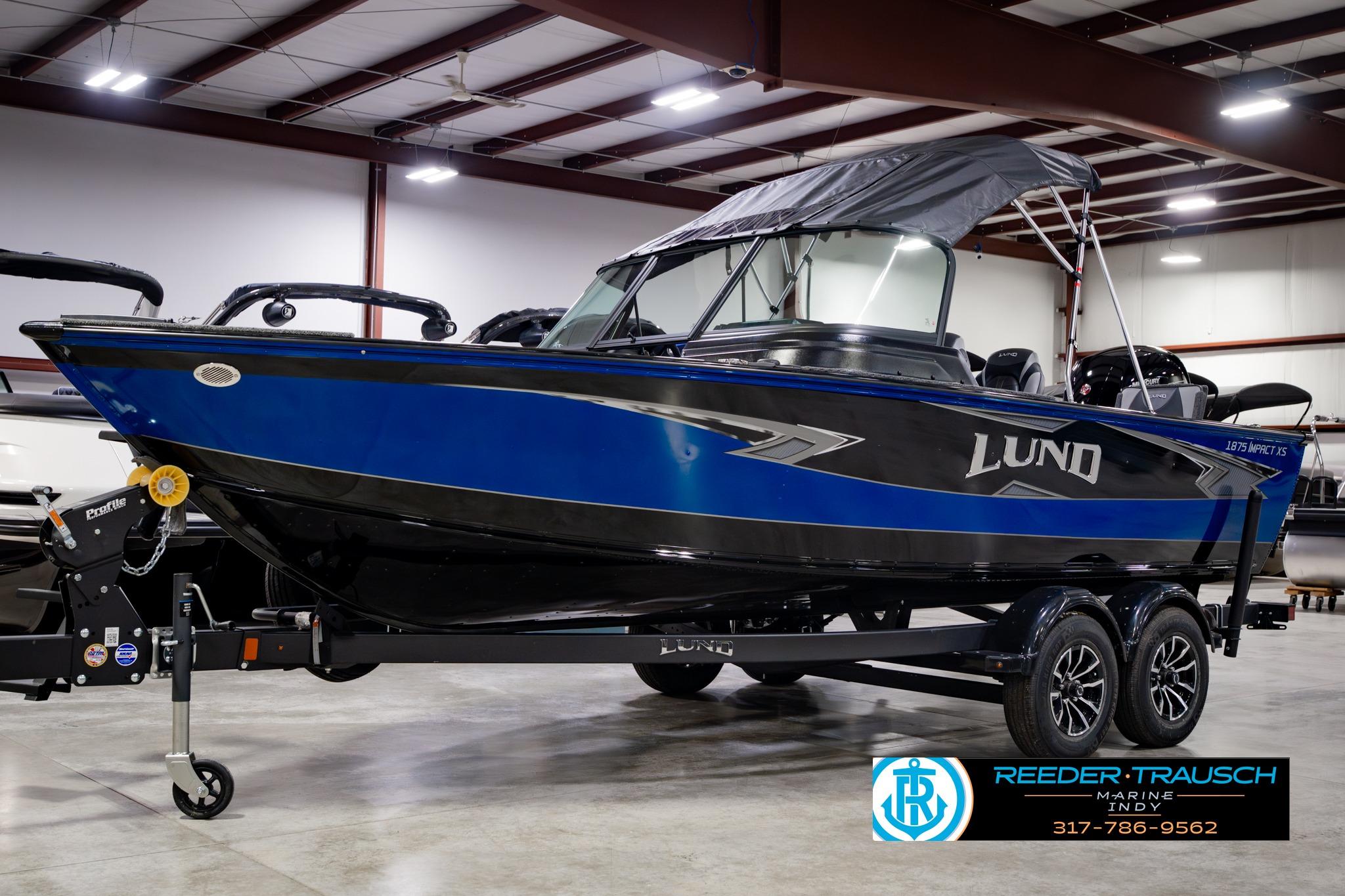 2026 Lund 1875 Impact XS boat in showroom, blue and black design, on trailer.