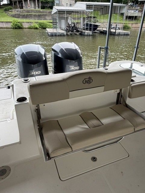 A boat with two outboard motors on calm water, featuring a seat in the foreground.