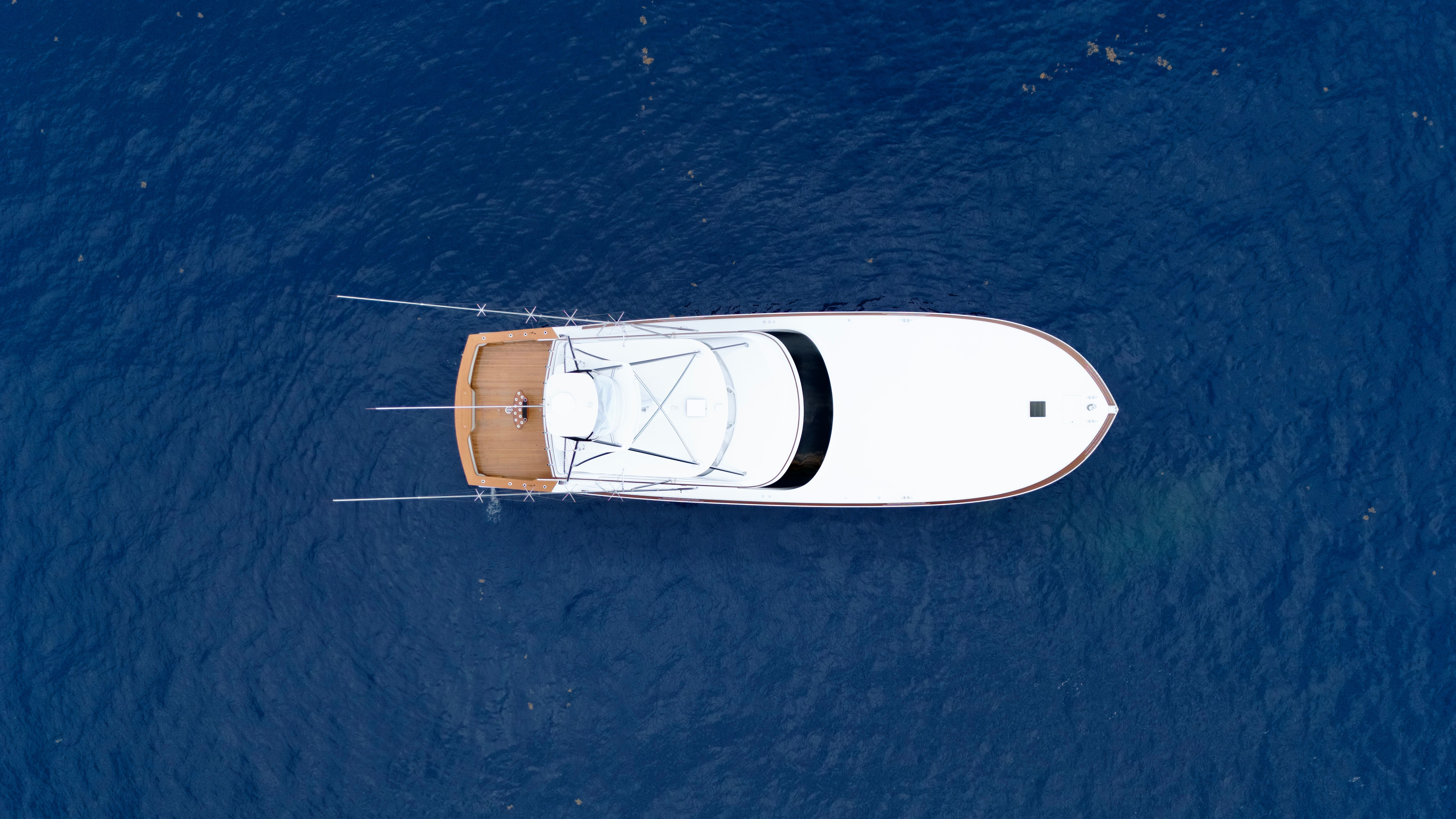 Aerial view of a white sportfishing yacht on blue water, featuring an open deck and antennas.