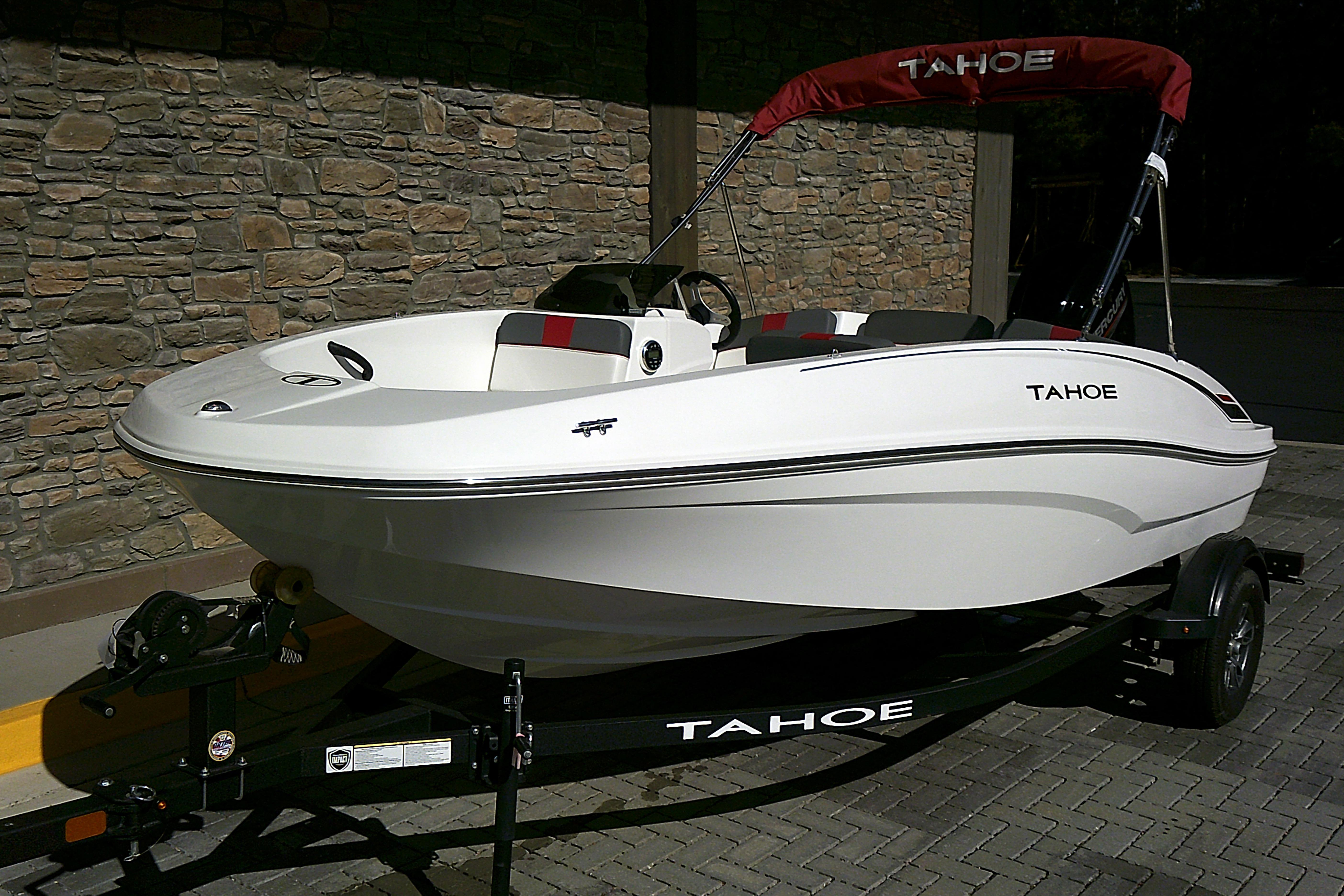 2025 Tahoe T16 boat on trailer, parked by stone wall, featuring sleek white design.