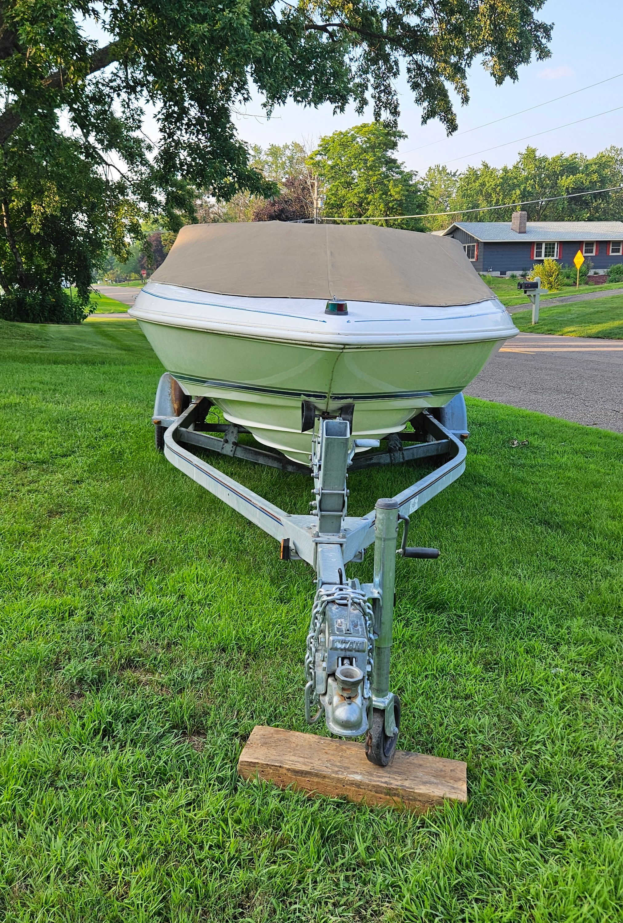 A 1996 Wellcraft Excel boat on a trailer, parked on a grassy lawn.