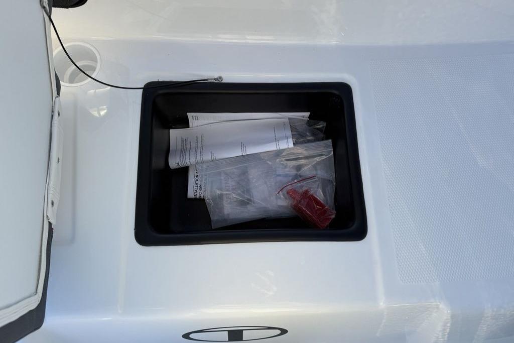 Open storage compartment in 2026 Tahoe T16 boat with documents and accessories.