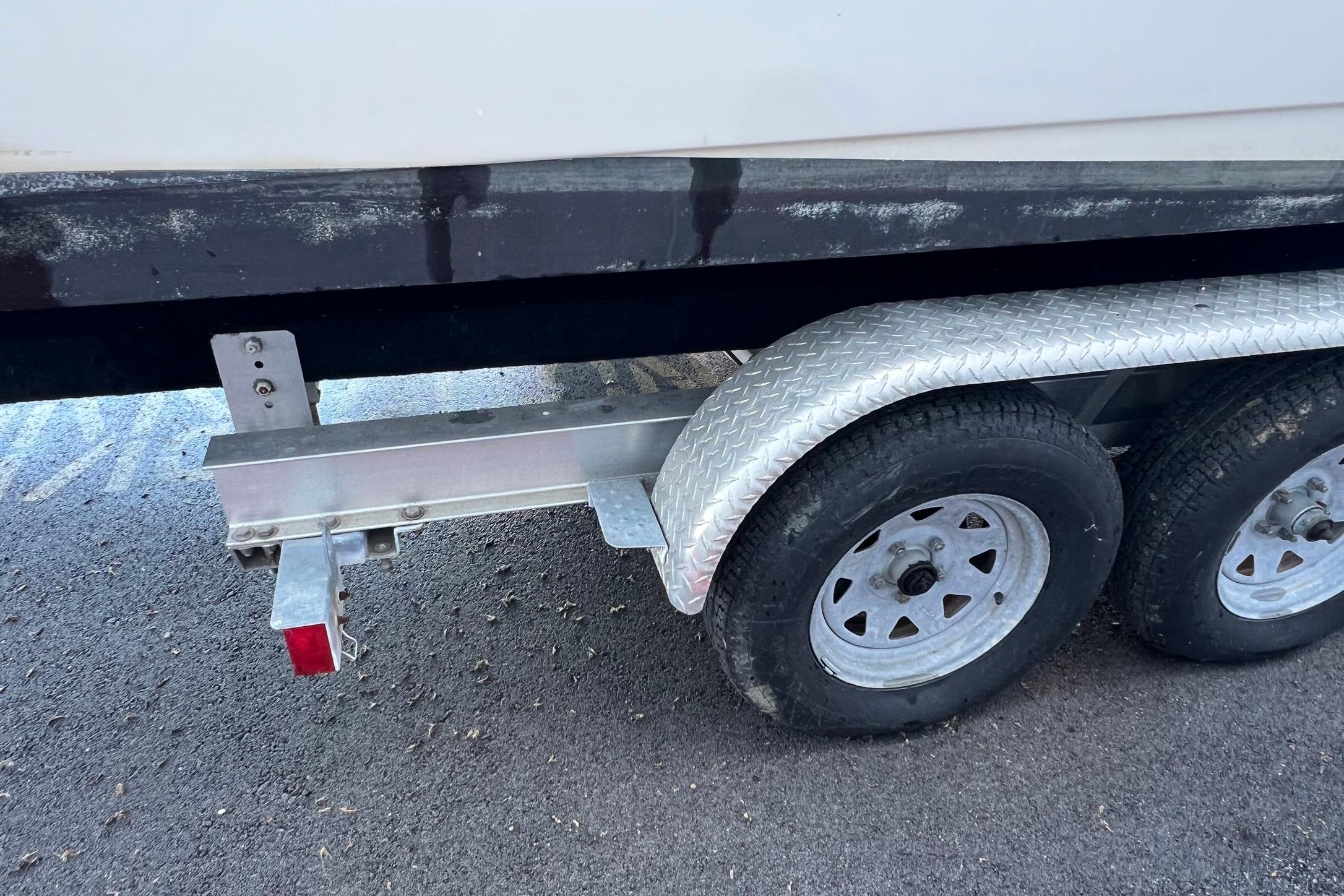 Trailer with dual wheels for 2006 Edgewater 245CC boat on asphalt surface.