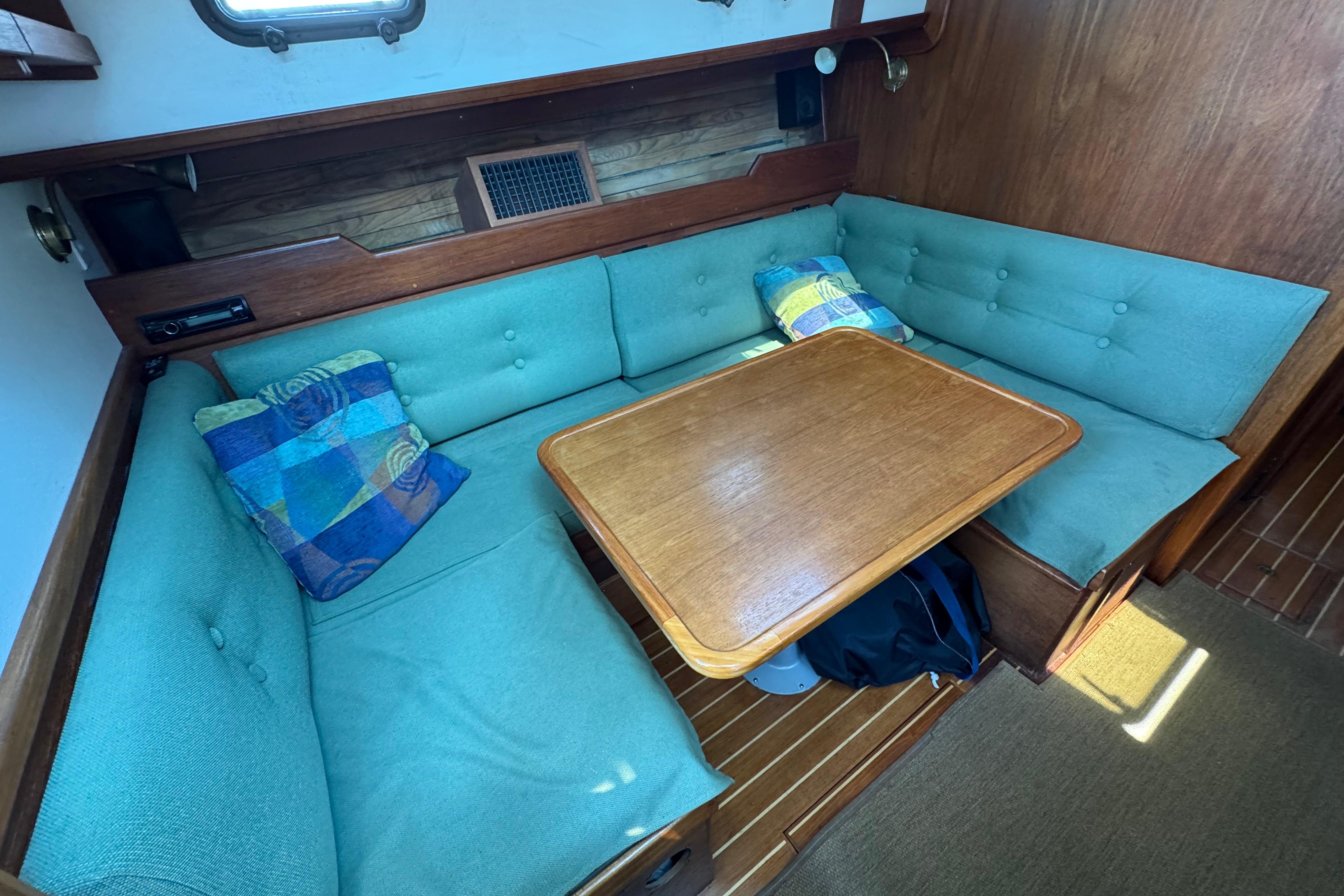 Cozy interior of 1989 Cape Dory 30 Motorsailer with teal seating and wooden table.